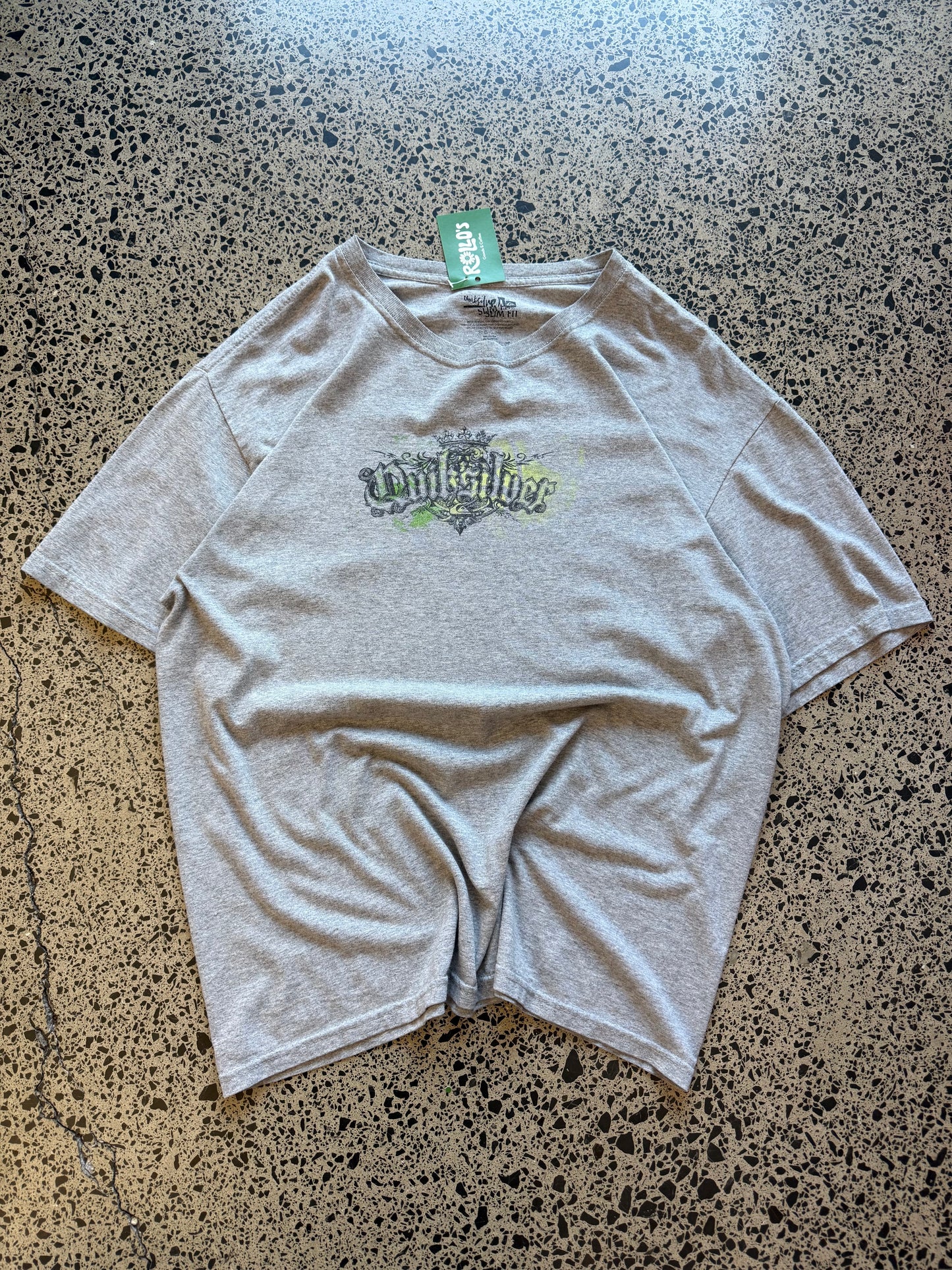 Grey early 2000s Quiksilver graphic t-shirt with chest and back logo print, size L, laid flat on a polished concrete background