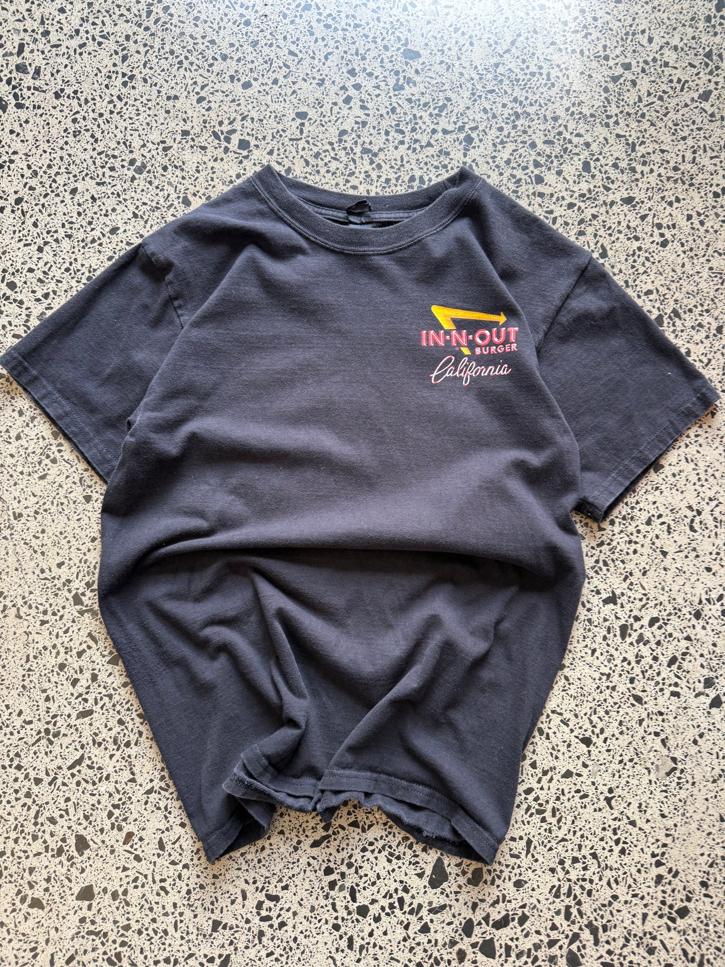 In-N-Out graphic T-shirt, size S, laid on polished concrete background — soft cotton with bold front logo print.