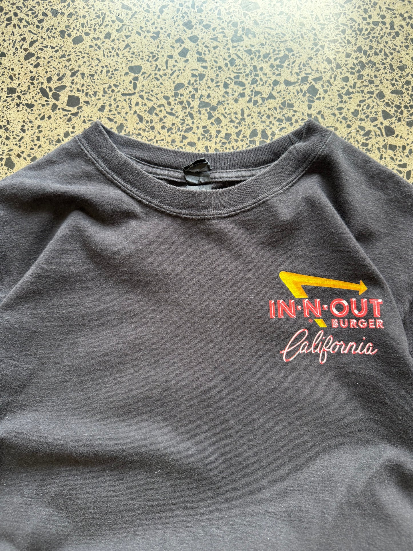 In-N-Out graphic T-shirt, size S, laid on polished concrete background — soft cotton with bold front logo print.