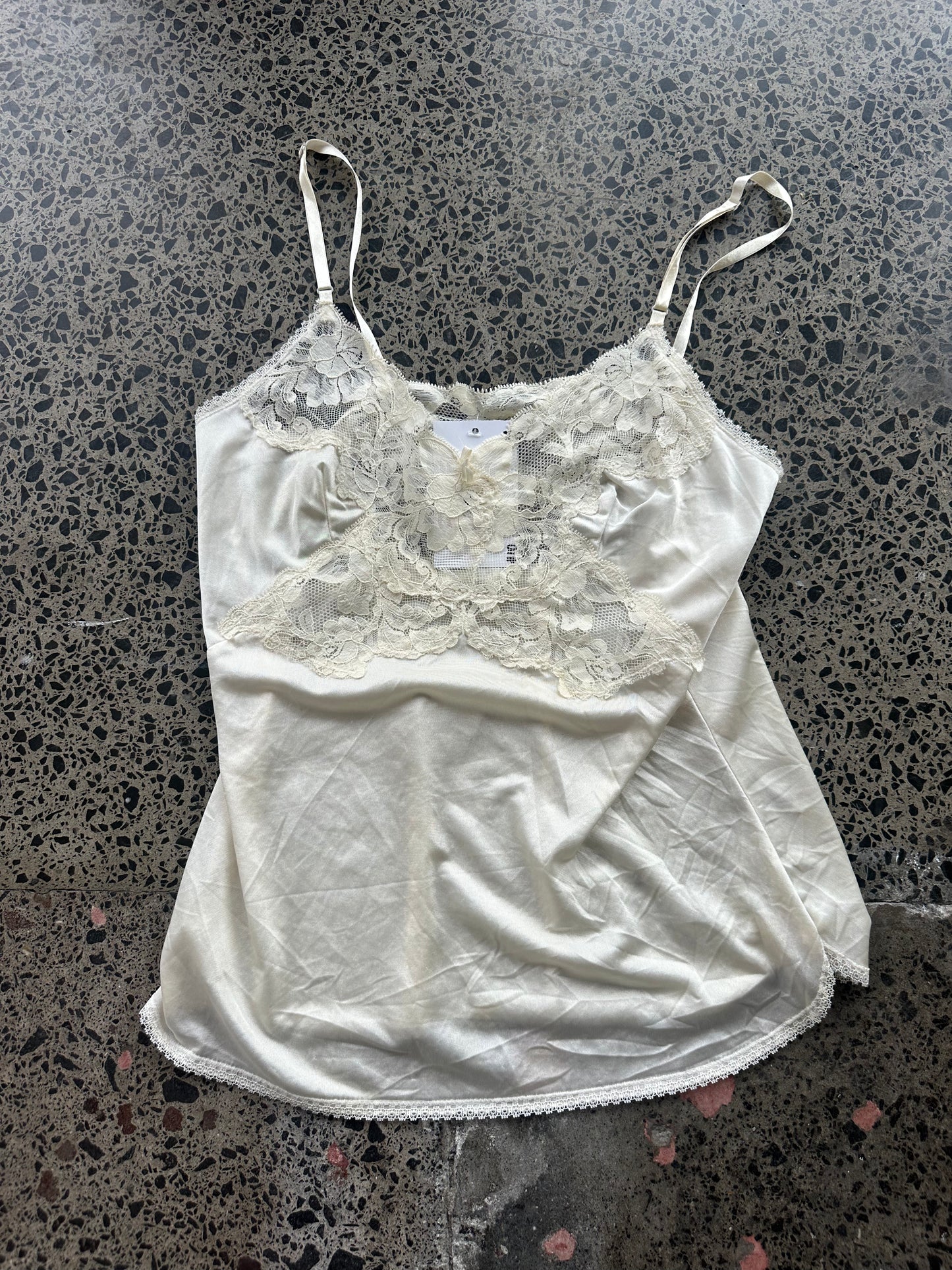 White satin camisole with lace detailing on a textured surface