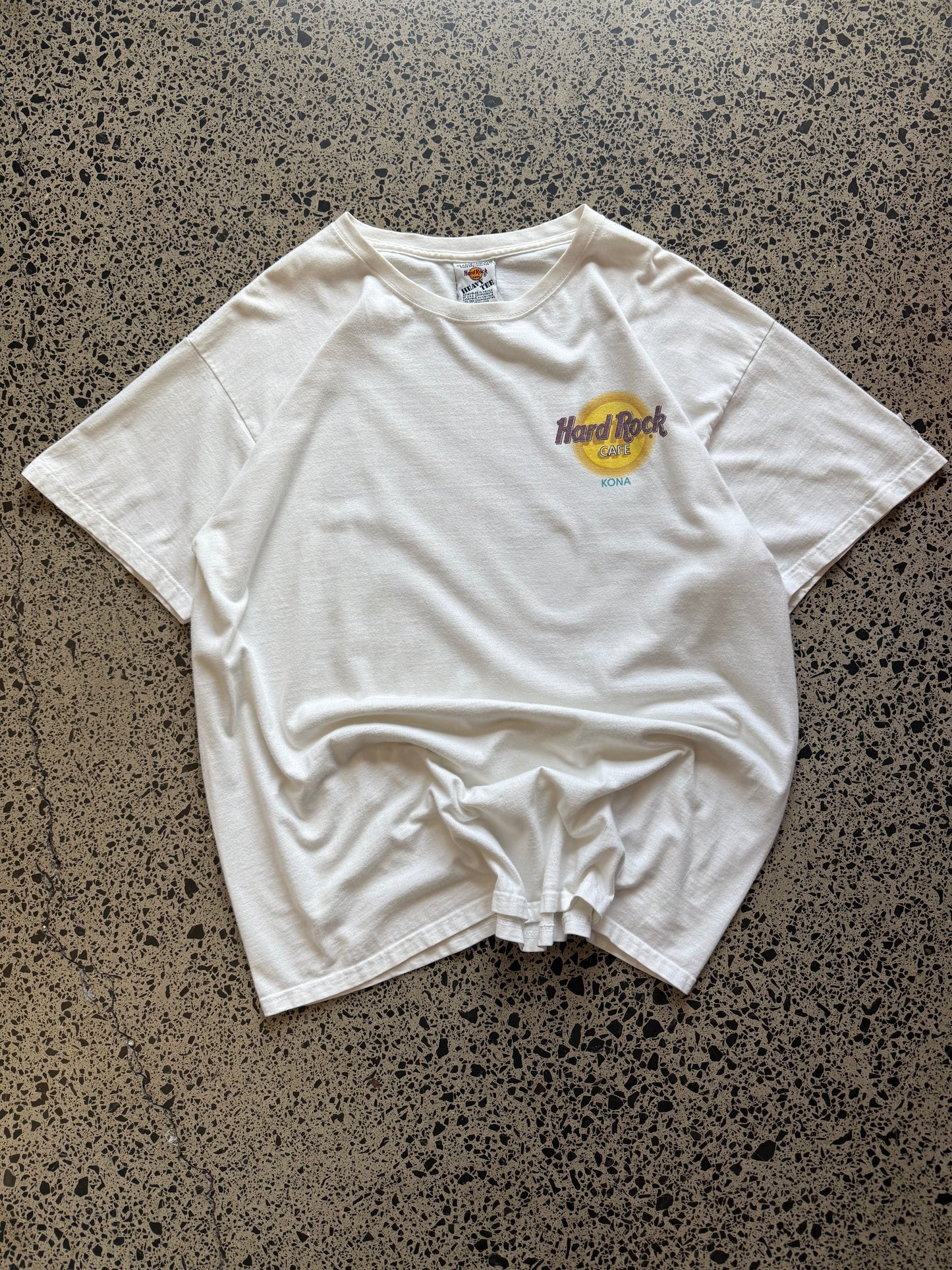 White 80s Hard Rock Kona graphic t-shirt with multicoloured print, size XL, laid flat on a polished concrete background