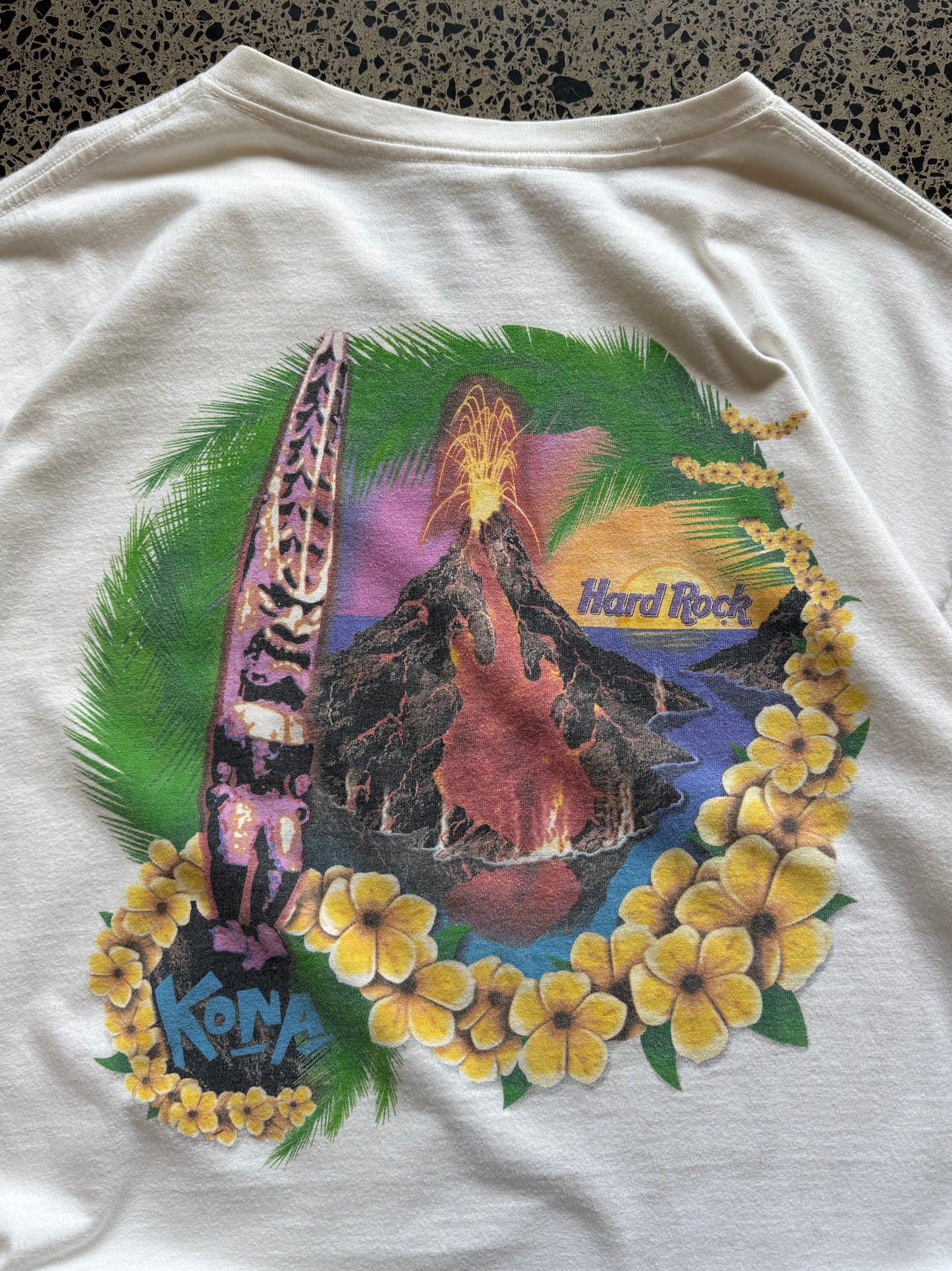 White 80s Hard Rock Kona graphic t-shirt with multicoloured print, size XL, laid flat on a polished concrete background