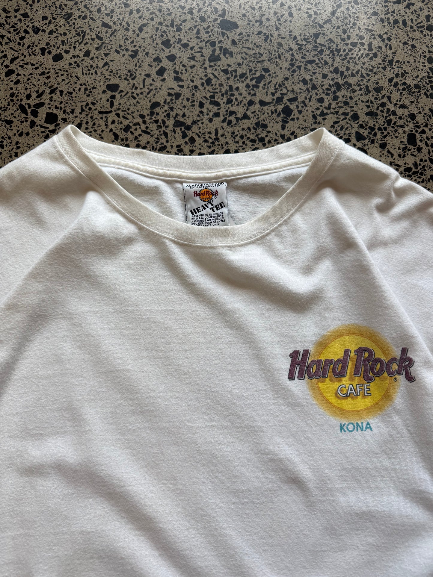 White 80s Hard Rock Kona graphic t-shirt with multicoloured print, size XL, laid flat on a polished concrete background