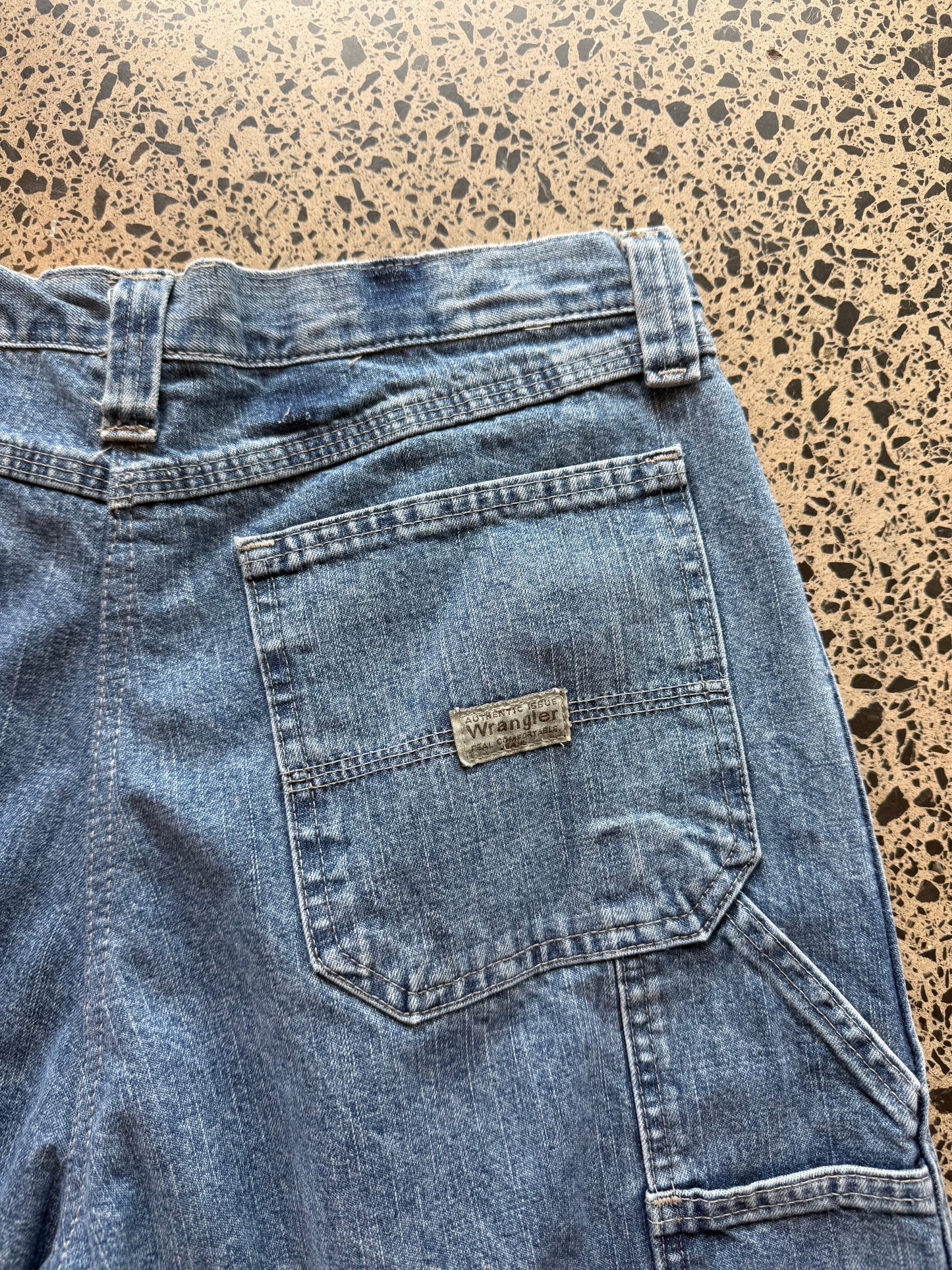 Wrangler mid blue wash denim jorts, size 30W, laid on polished concrete background. Knee cut with classic stitching and soft wash