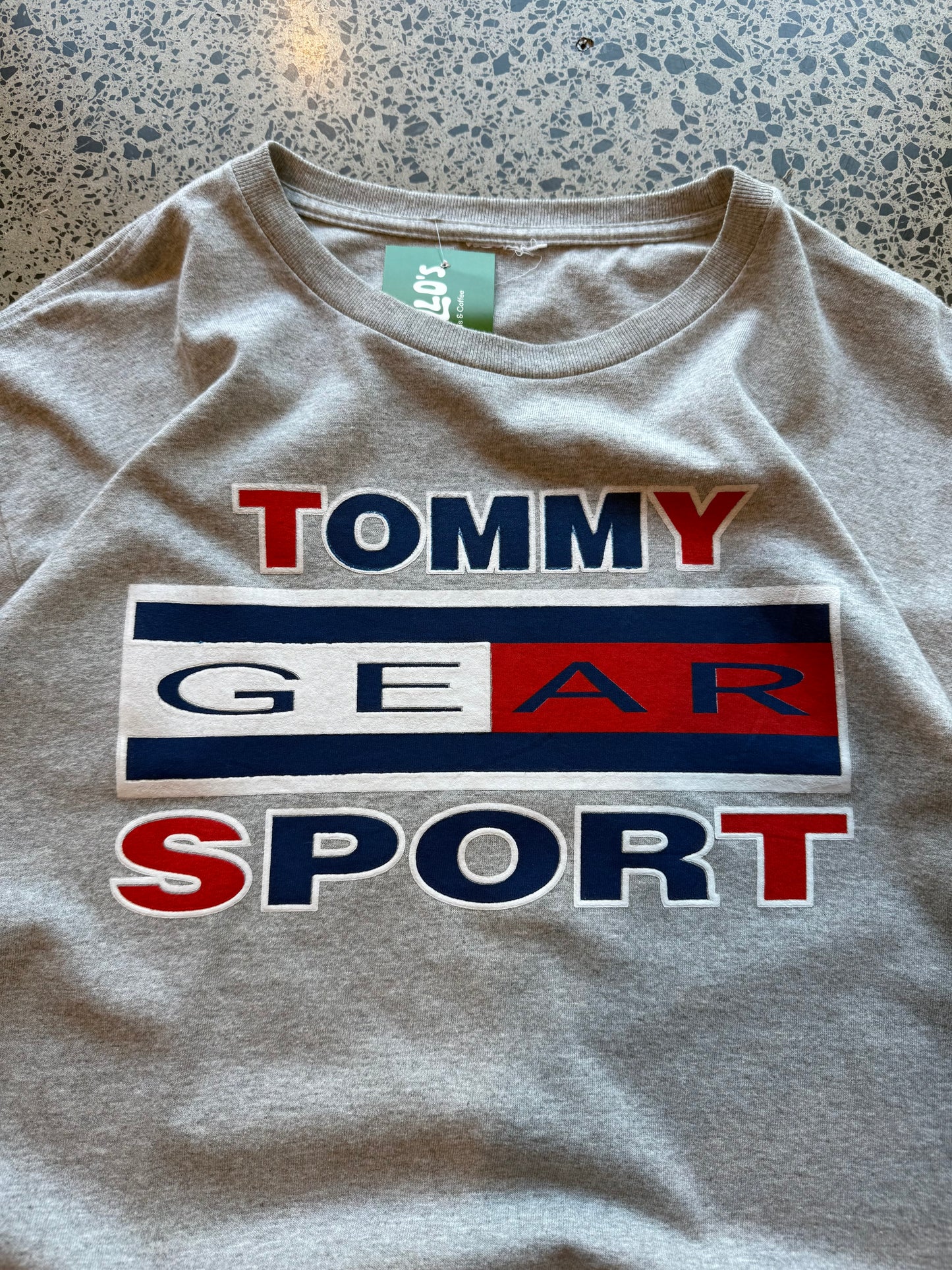 2000s Tommy Hilfiger T-shirt in size L laid on a polished concrete background with small front logo.