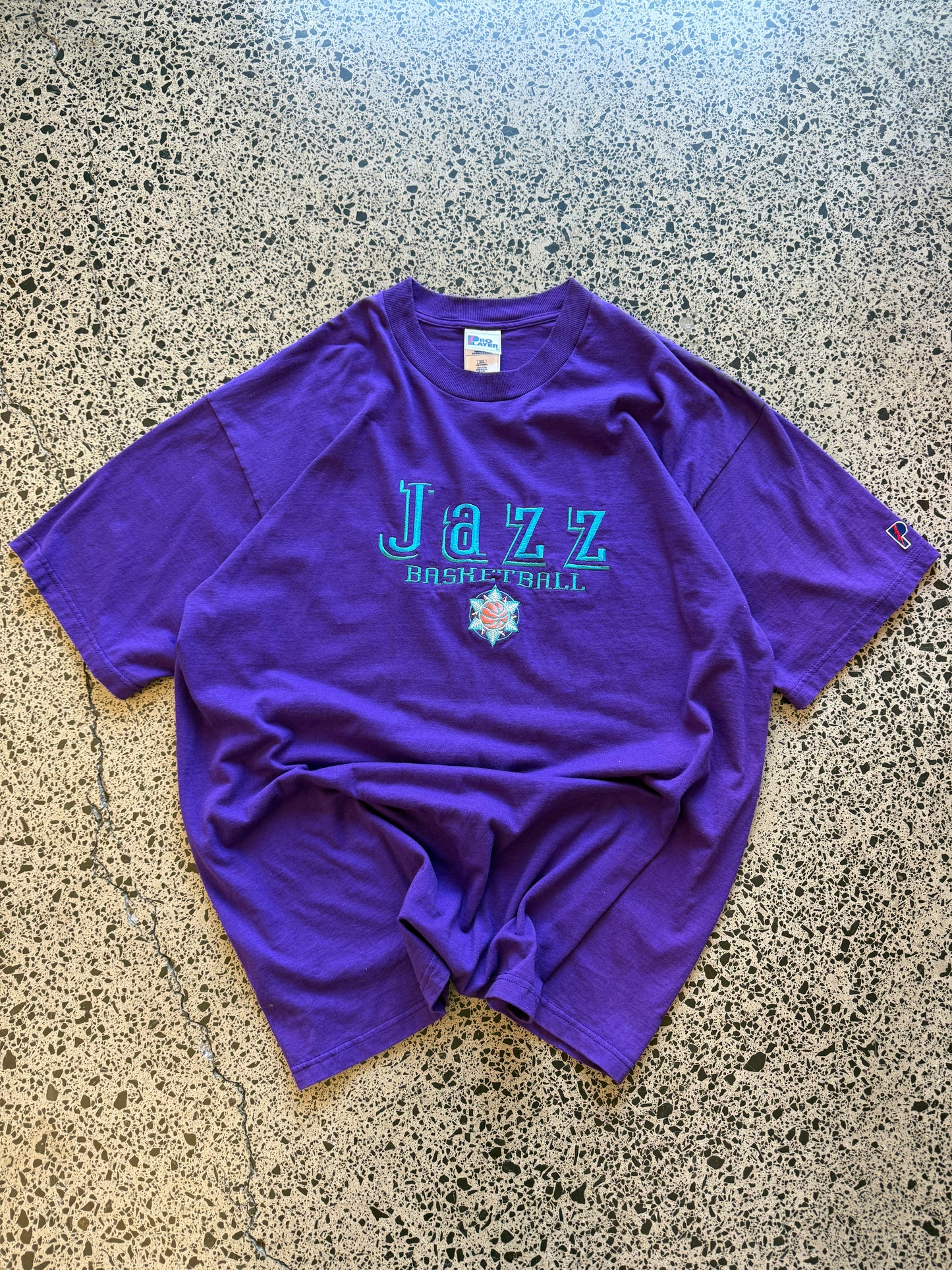 Vintage 90s Utah Jazz NBA t-shirt on a purple base and blue team logos and graphics embroidered across the front. Size 2XL. Oversized basketball streetwear