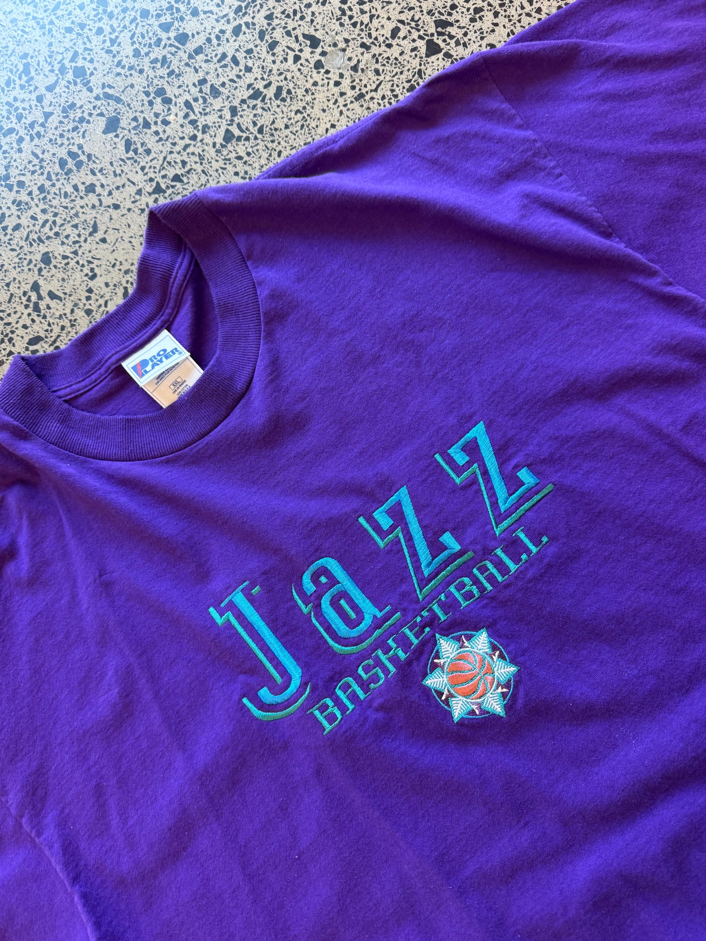 Vintage 90s Utah Jazz NBA t-shirt on a purple base and blue team logos and graphics embroidered across the front. Size 2XL. Oversized basketball streetwear