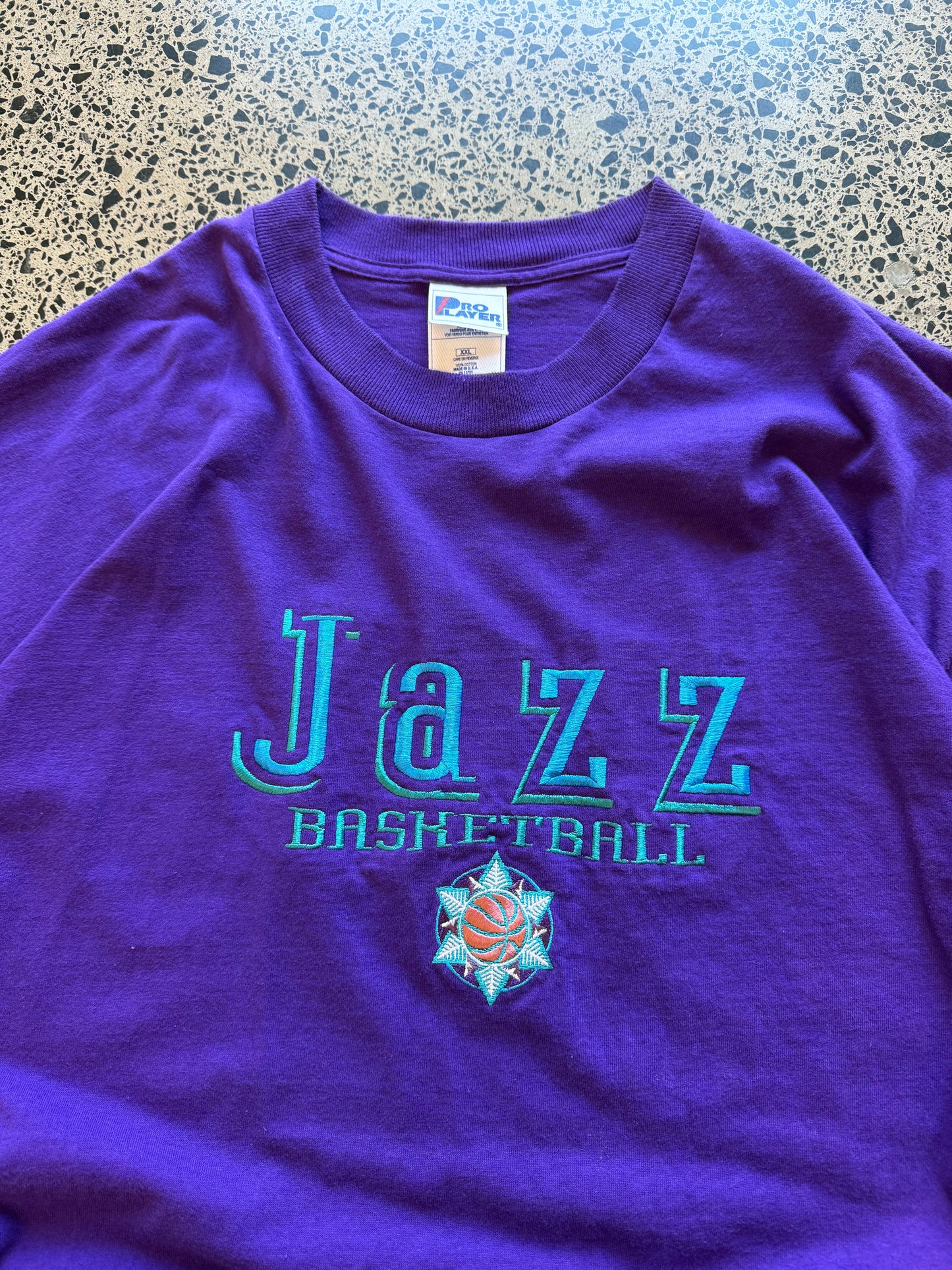 Vintage 90s Utah Jazz NBA t-shirt on a purple base and blue team logos and graphics embroidered across the front. Size 2XL. Oversized basketball streetwear