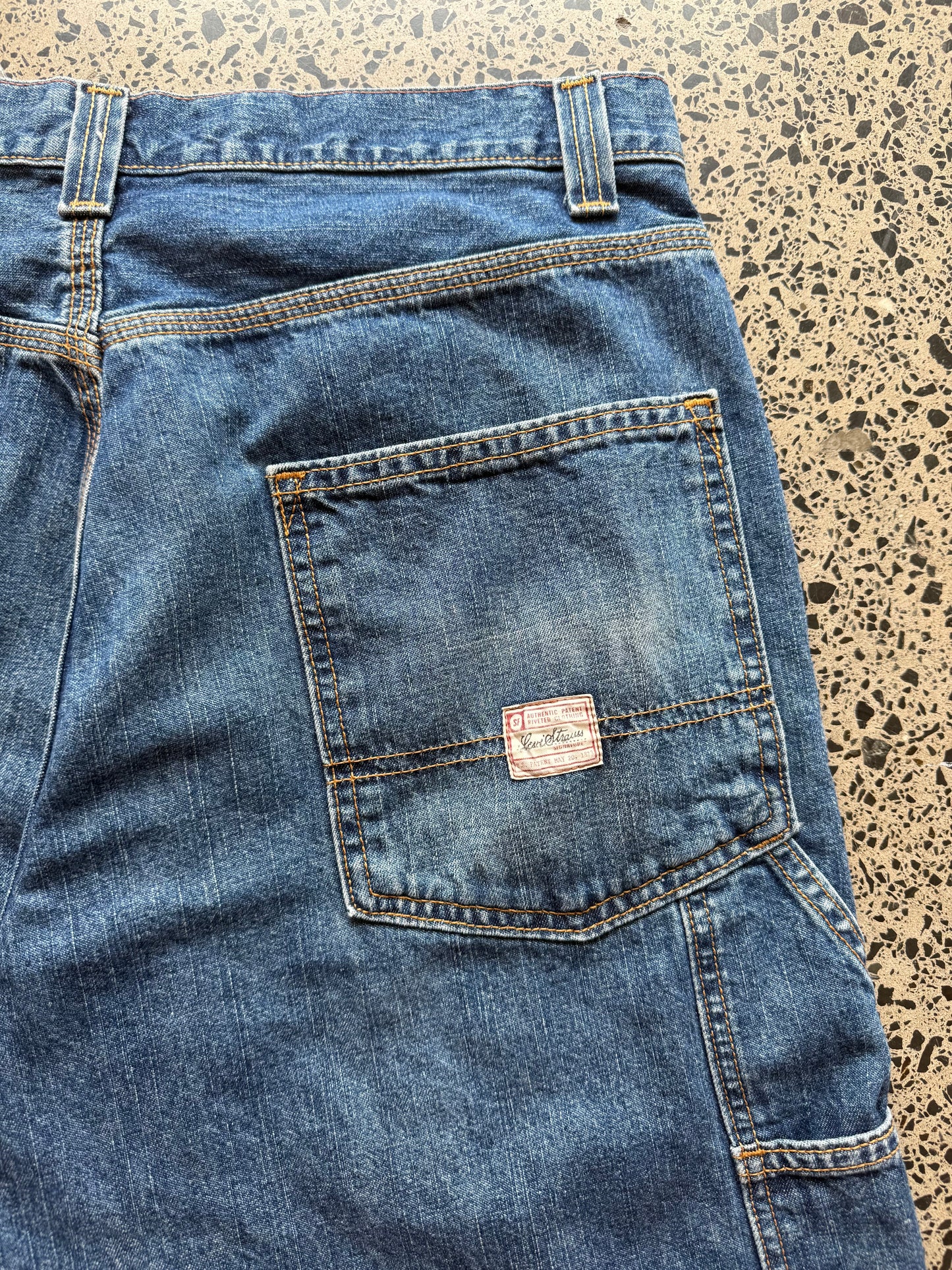 Levi strauss dark blue wash denim jorts, size 32W, laid on polished concrete background. Knee cut with classic stitching and soft wash