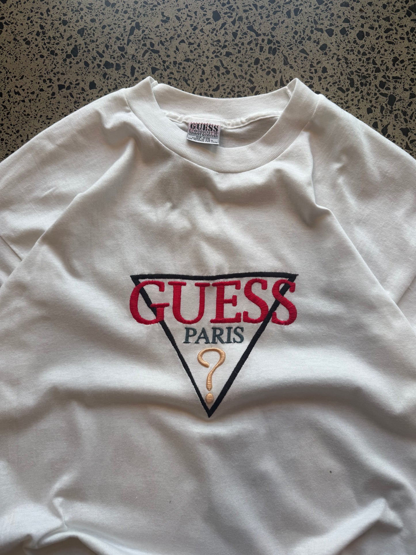 90s Guess embroidered logo T-shirt, size XL, laid on polished concrete background — vintage cotton tee with stitched Guess branding.