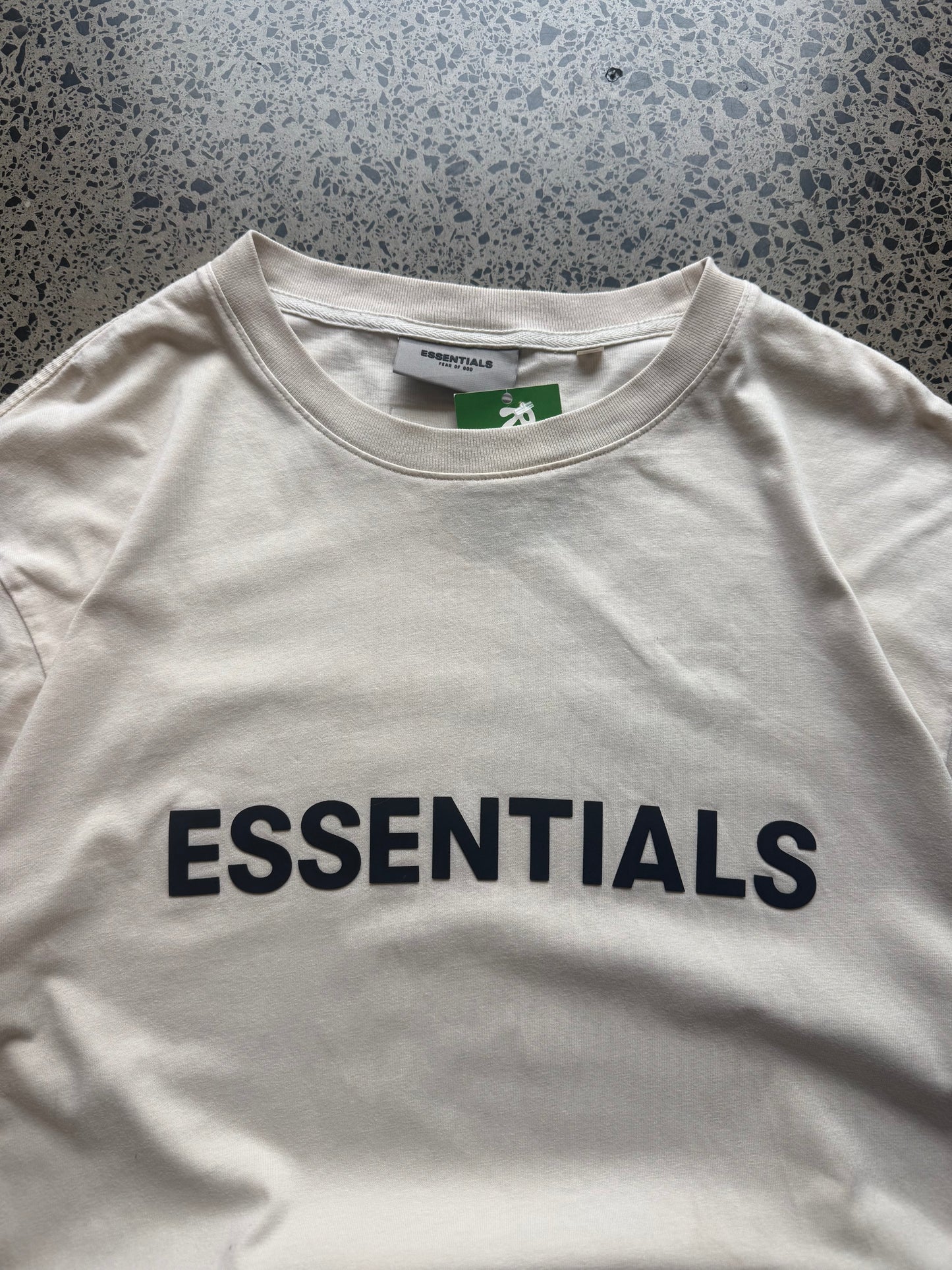 Fear of God Essentials t-shirt size M laid flat on polished concrete background, minimal streetwear tee with subtle Essentials branding and relaxed fit.