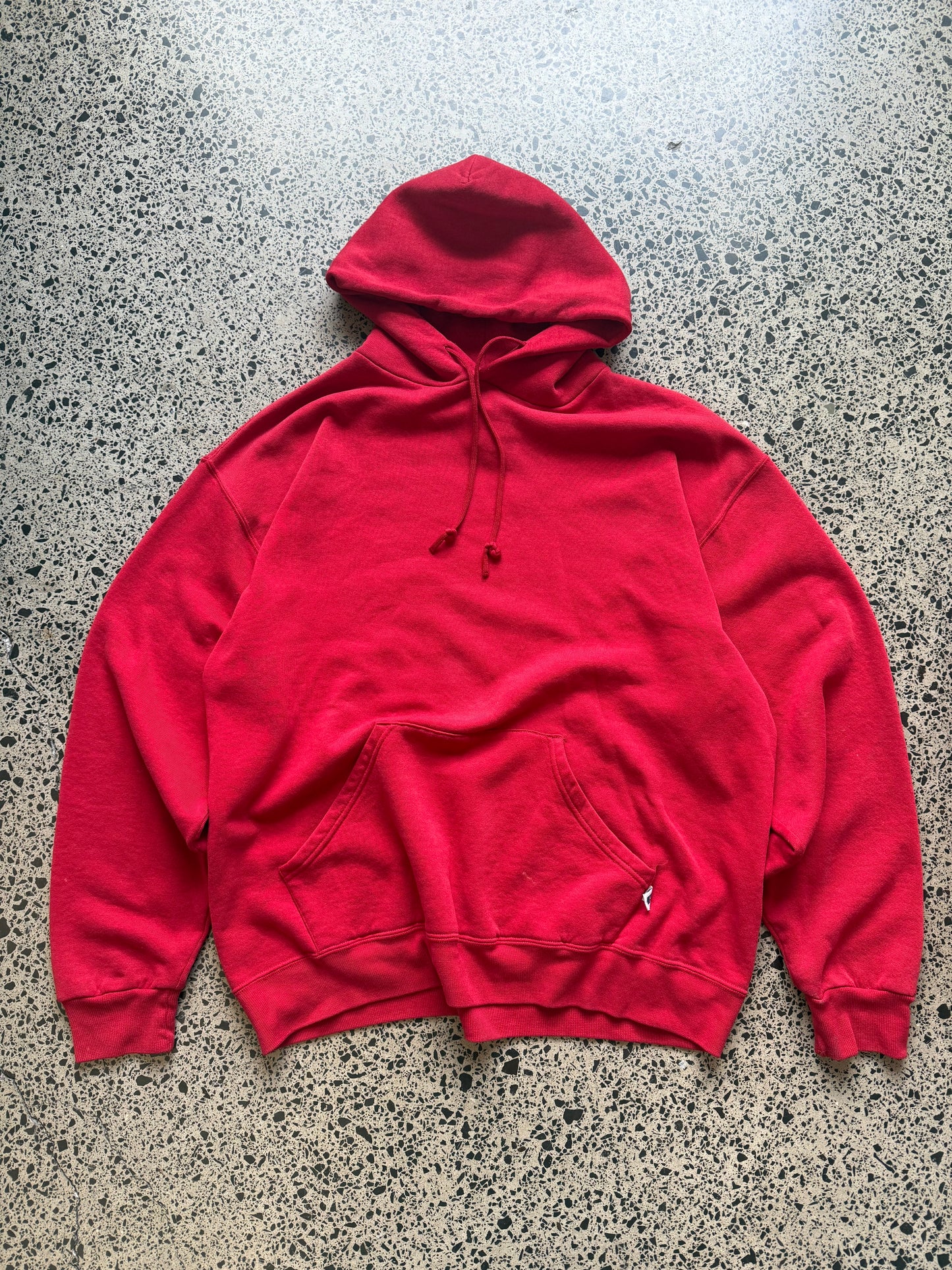 Russell Athletic blank hoodie size L laid on polished concrete background — red hoodie