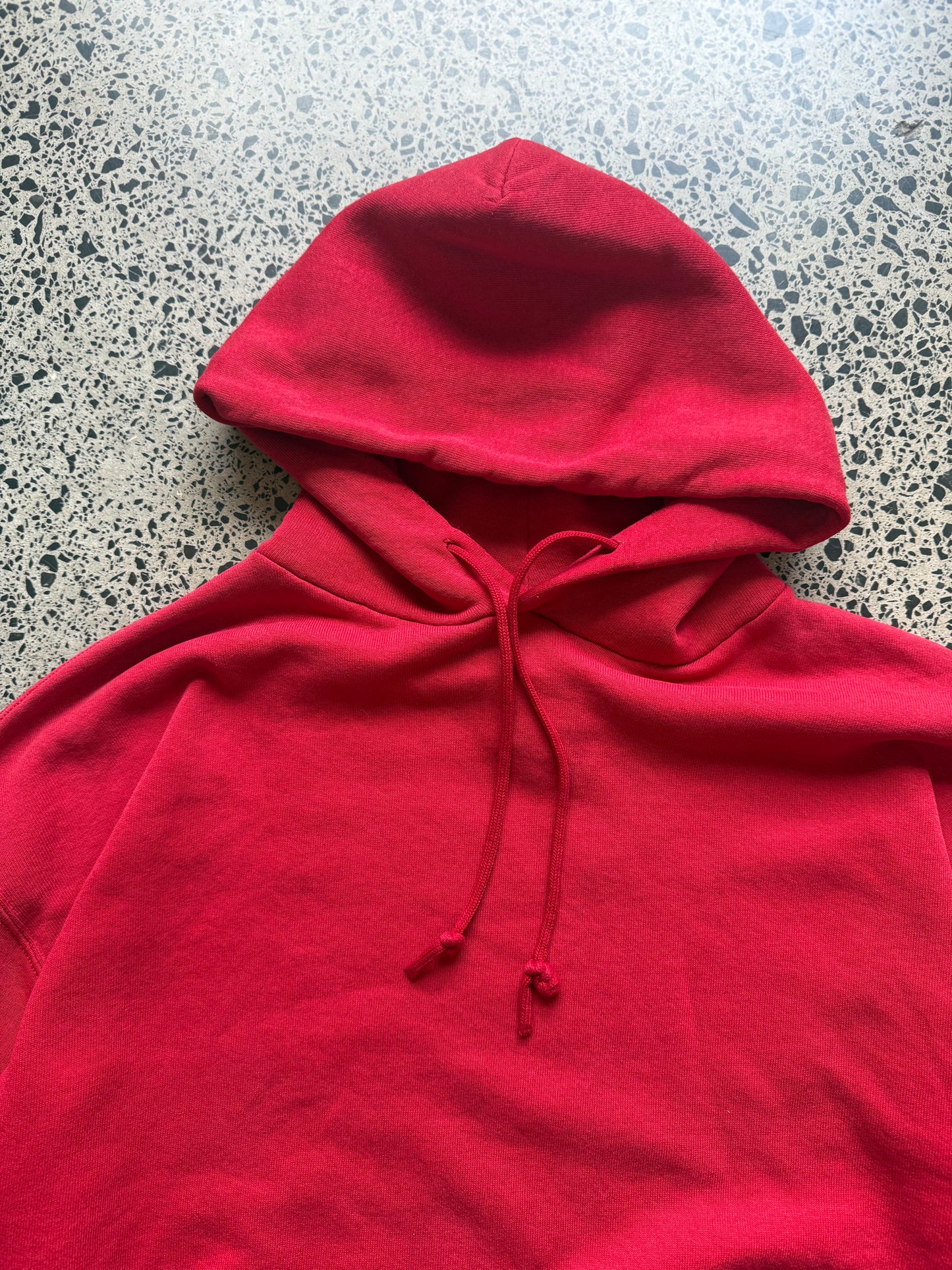 Russell Athletic blank hoodie size L laid on polished concrete background — red hoodie