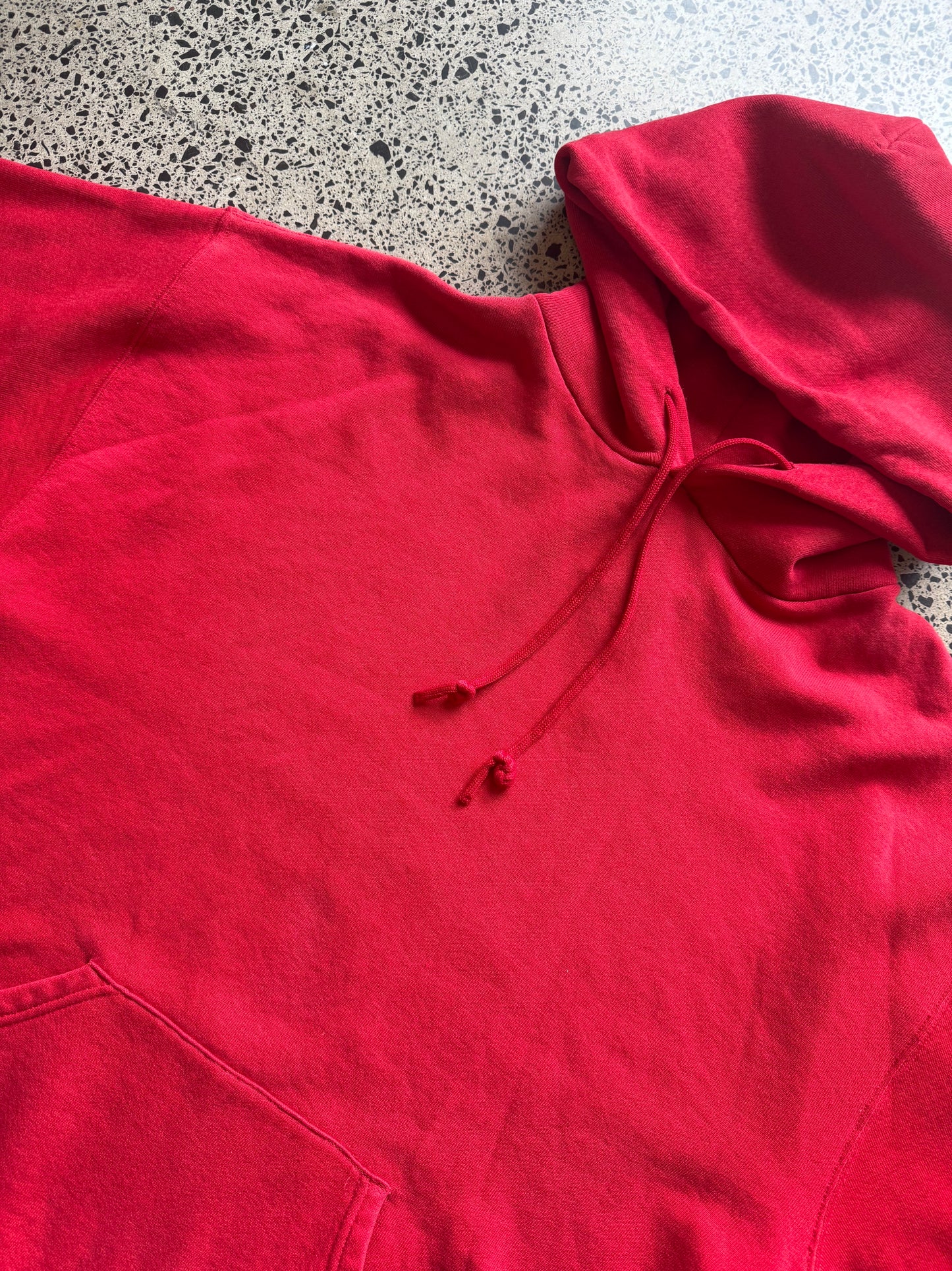 Russell Athletic blank hoodie size L laid on polished concrete background — red hoodie
