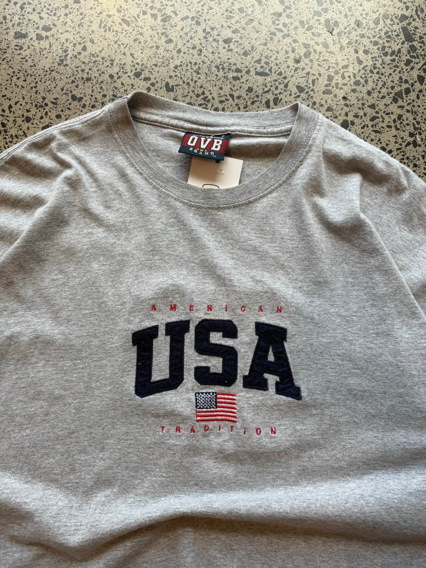 USA flag graphic T-shirt in size 2XL laid on a polished concrete background with vintage-style print.
