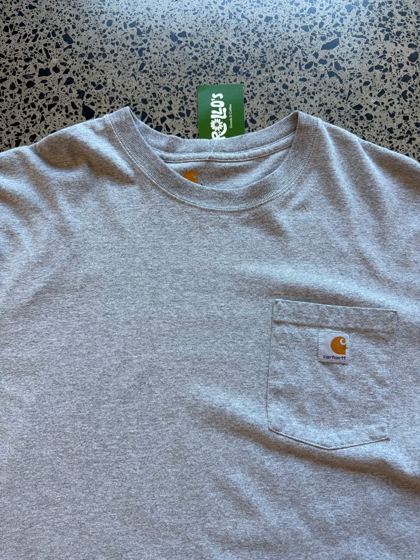 Grey Carhartt pocket t-shirt with chest logo patch, size L, laid flat on a polished concrete background