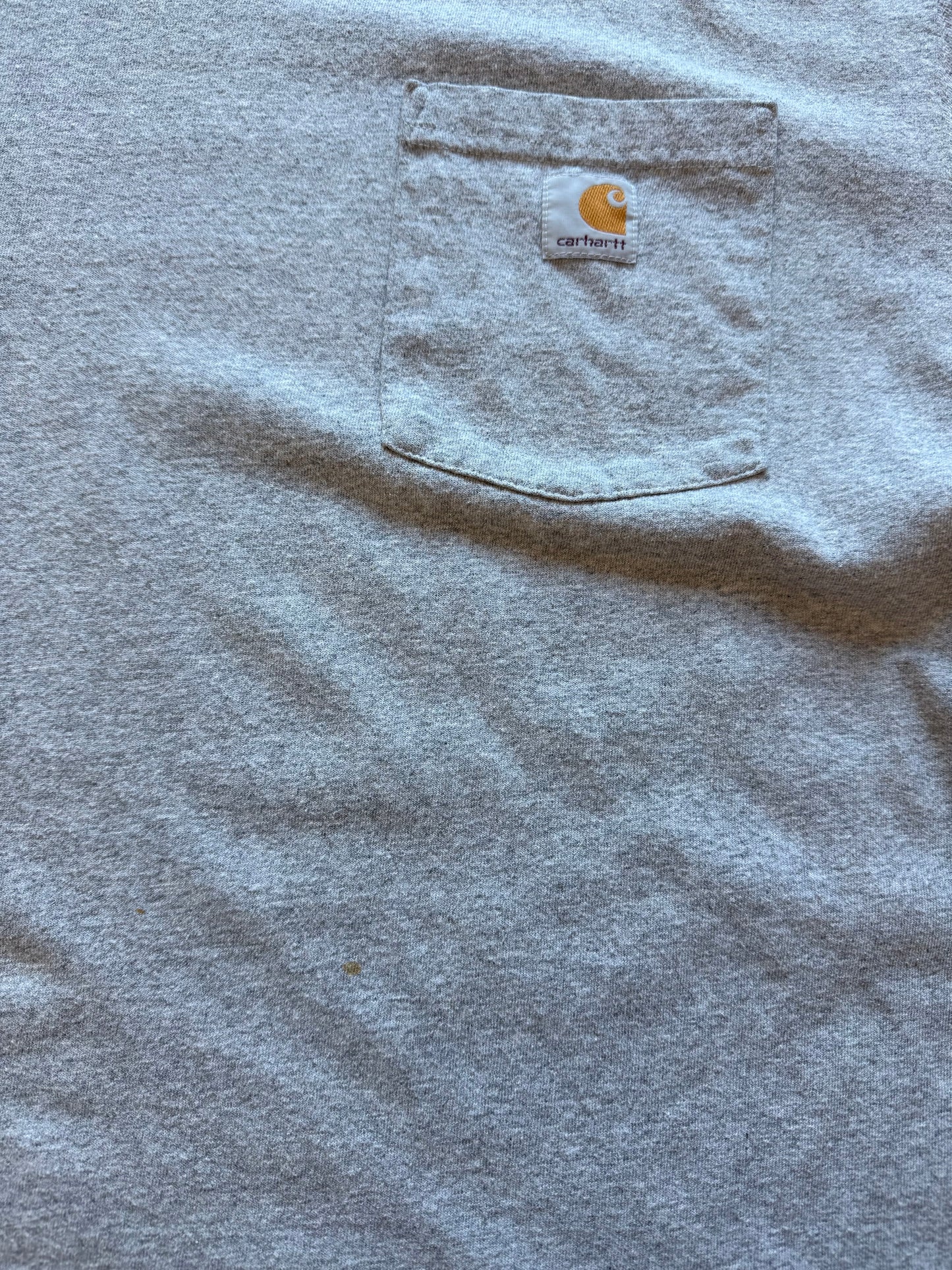 Grey Carhartt pocket t-shirt with chest logo patch, size L, laid flat on a polished concrete background