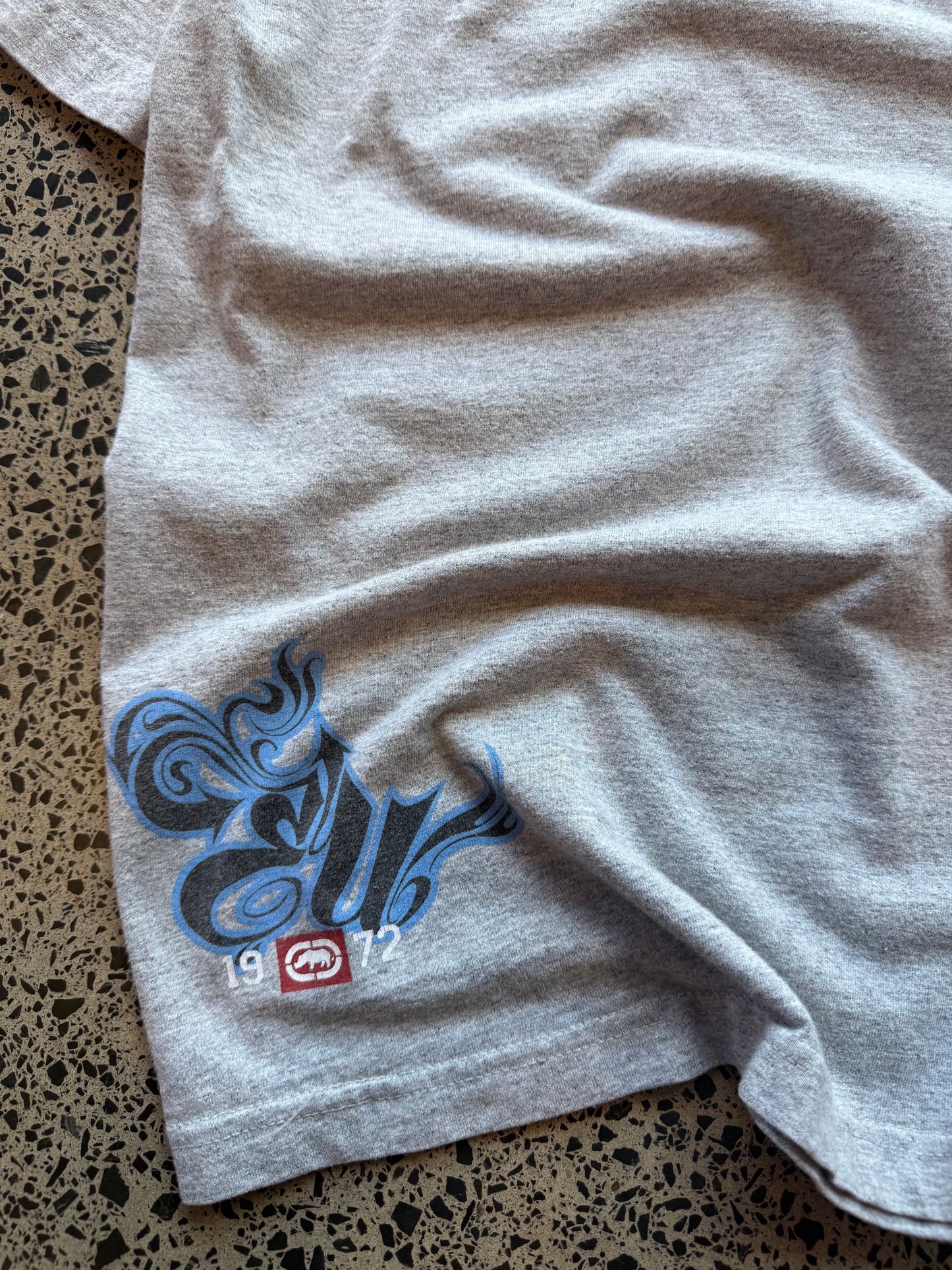 Ecko Unltd black graphic T-shirt in size L laid on a polished concrete background with large rhino logo on the front.