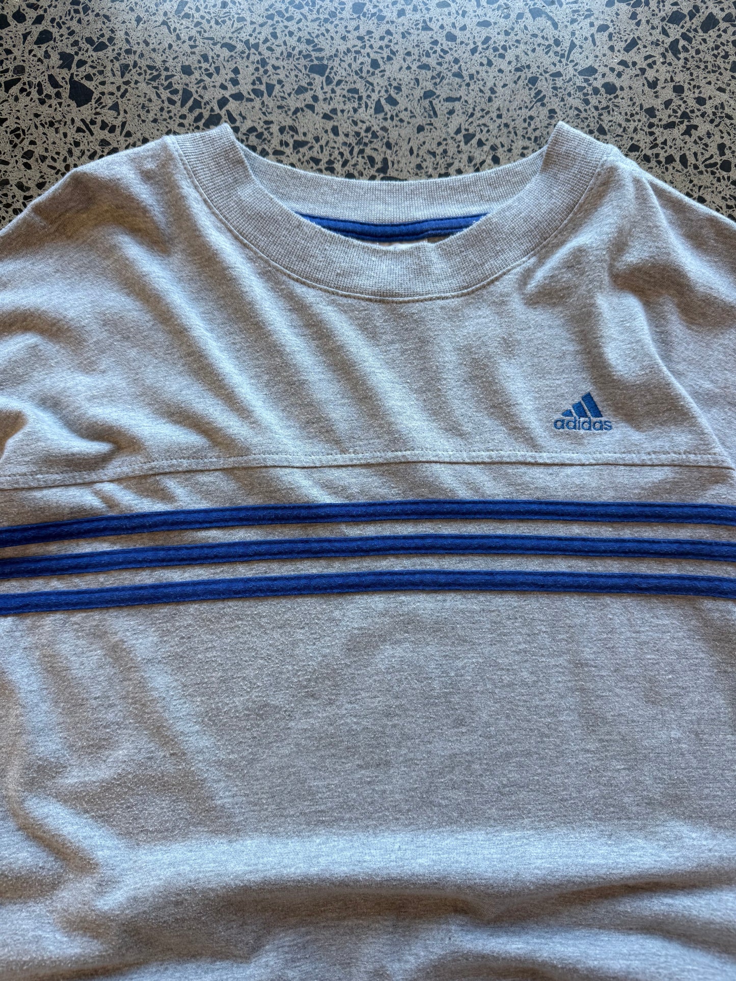 90s vintage Adidas essential T-shirt size XL laid on polished concrete background — black tee with Adidas logo.