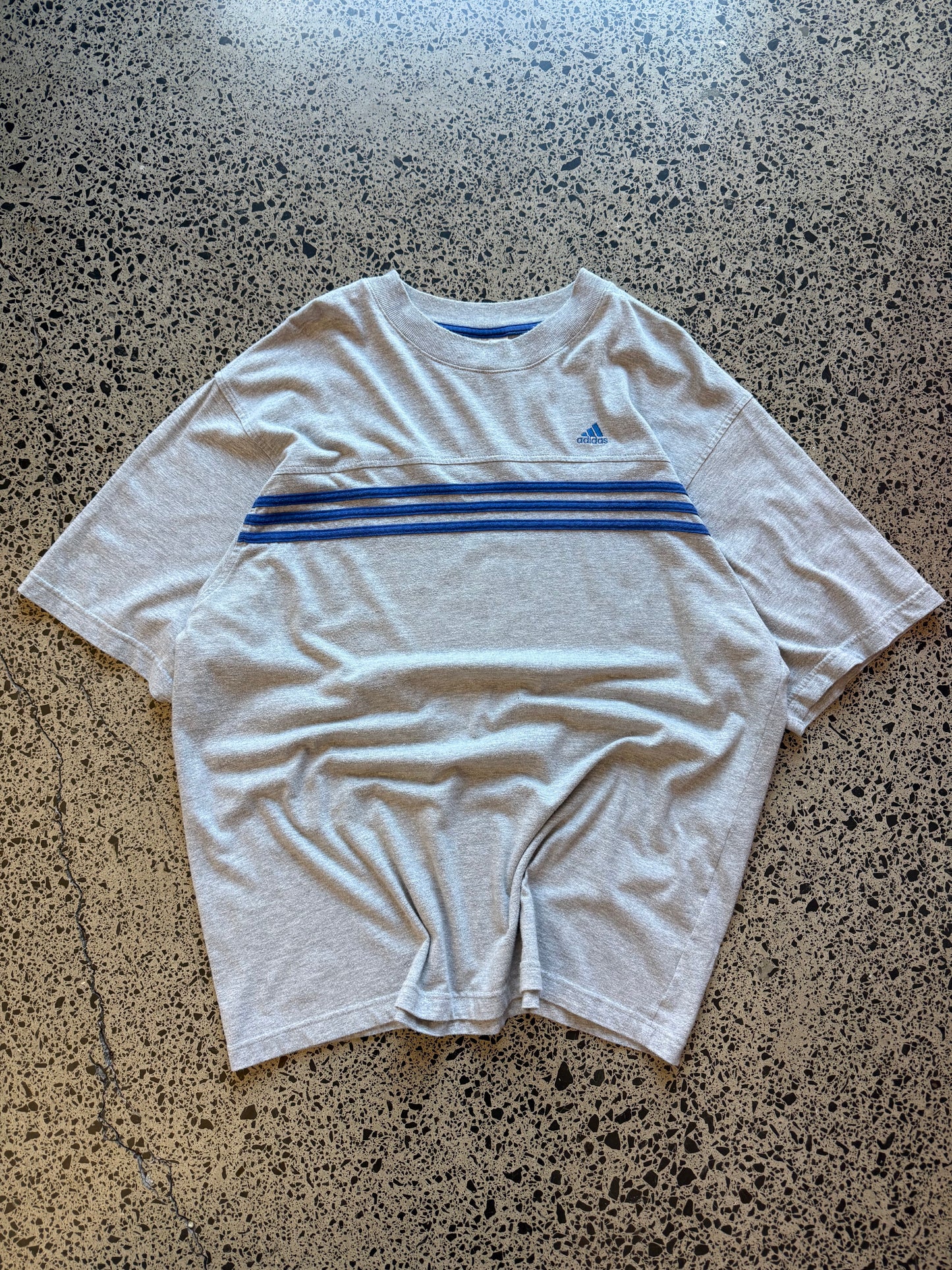 90s vintage Adidas essential T-shirt size XL laid on polished concrete background — black tee with Adidas logo.