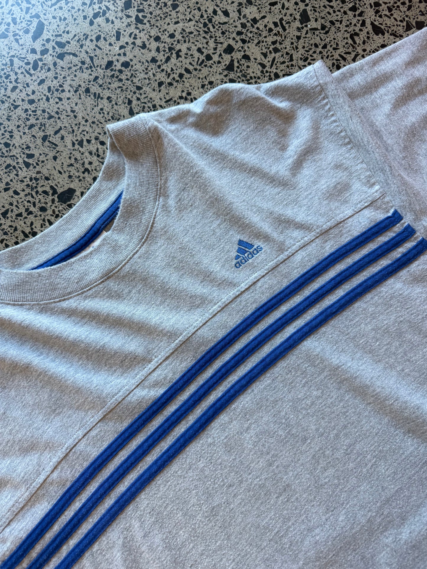 90s vintage Adidas essential T-shirt size XL laid on polished concrete background — black tee with Adidas logo.
