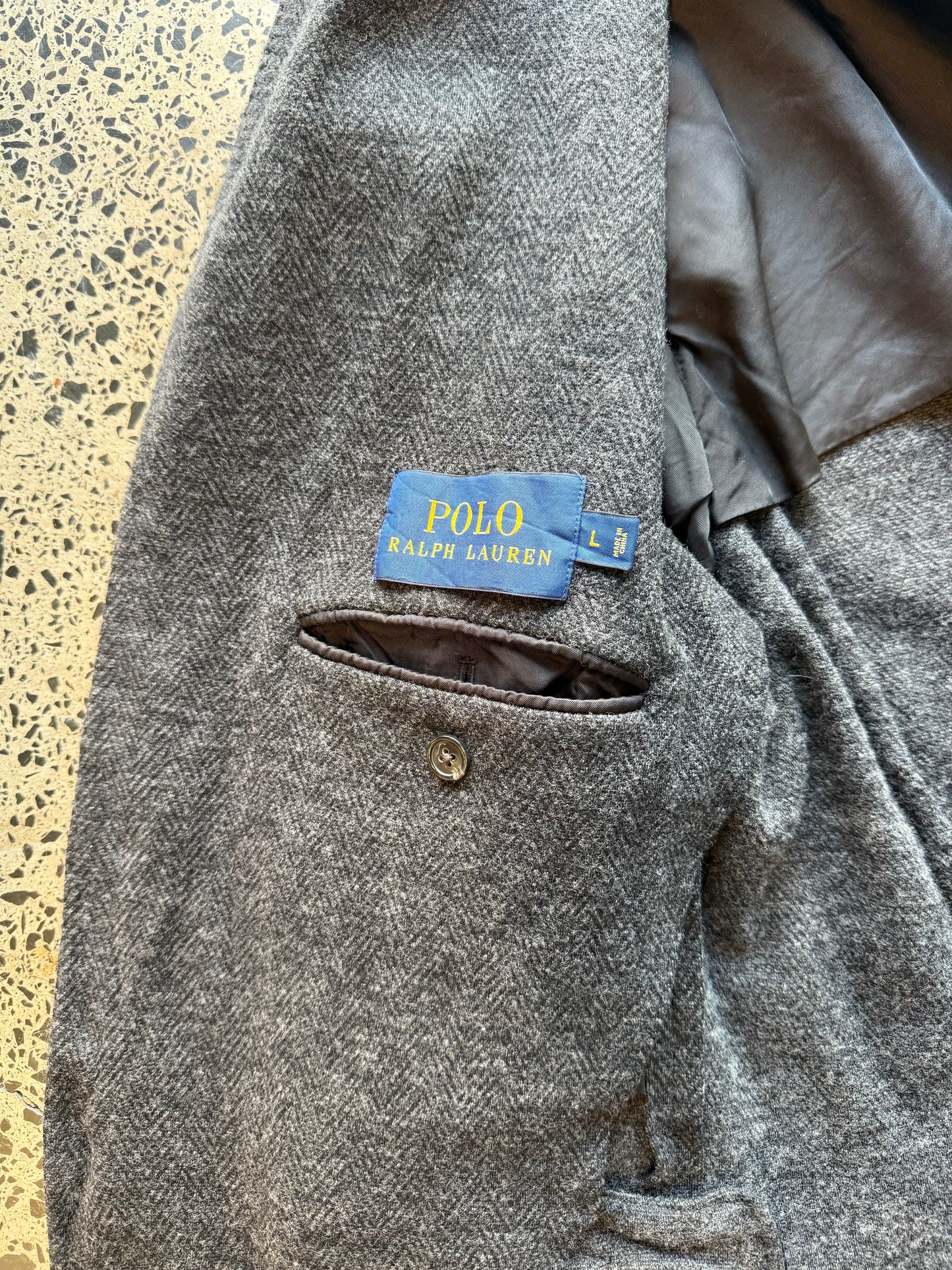 Ralph Lauren herringbone 100 percent wool blazer jacket laid flat on polished concrete background, classic tailored jacket with textured pattern and clean fit.