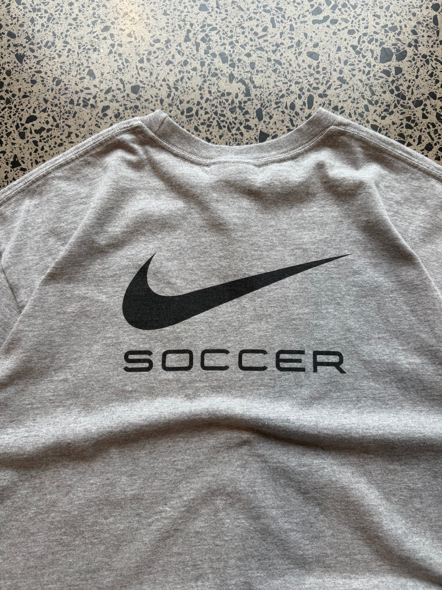 2000s Nike Abby Wambach Soccer Camp T-shirt in size M laid on a polished concrete background featuring U.S. women’s soccer camp graphic.