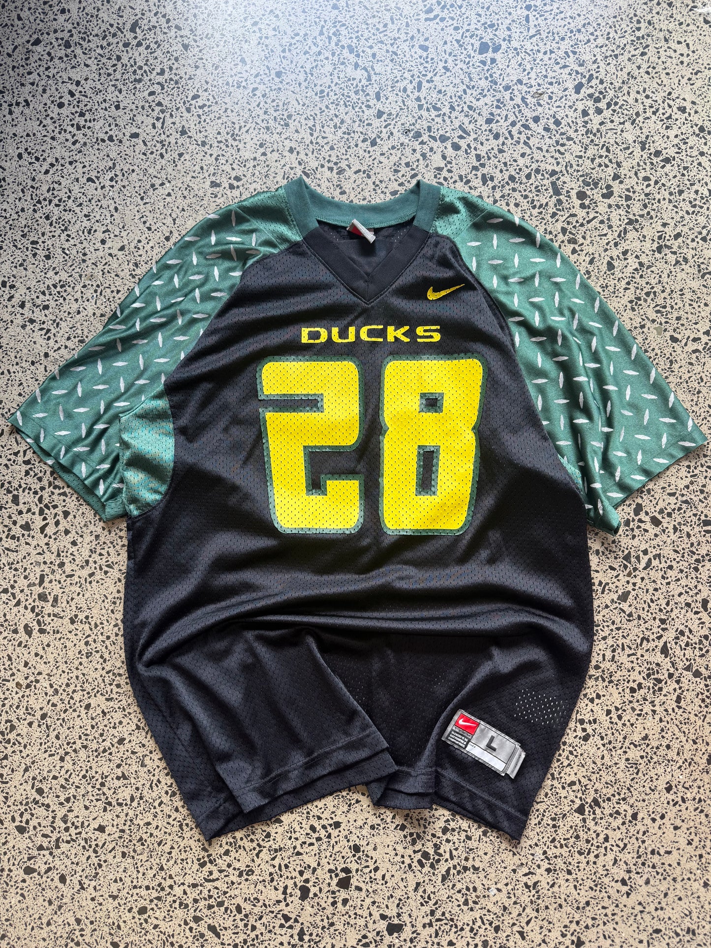 90s vintage Oregon Ducks jersey size L laid on polished concrete background — green with yellow detailing and Ducks logo.