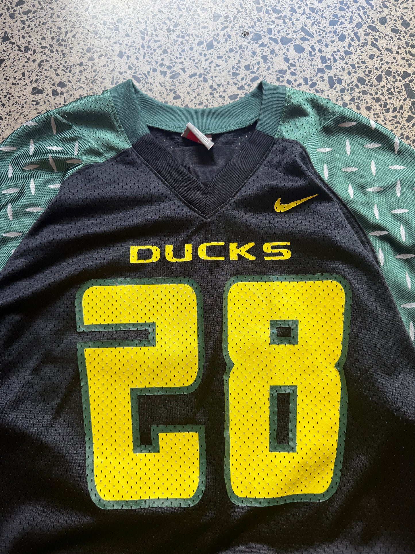 90s vintage Oregon Ducks jersey size L laid on polished concrete background — green with yellow detailing and Ducks logo.