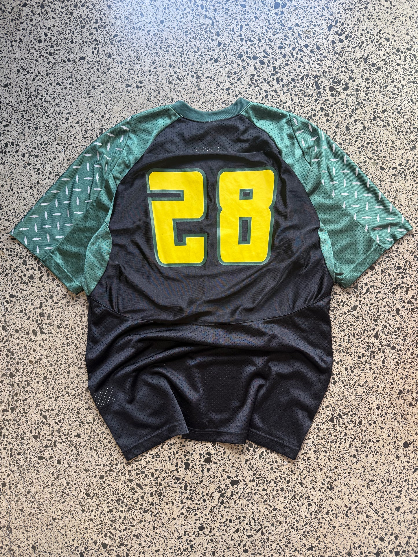 90s vintage Oregon Ducks jersey size L laid on polished concrete background — green with yellow detailing and Ducks logo.