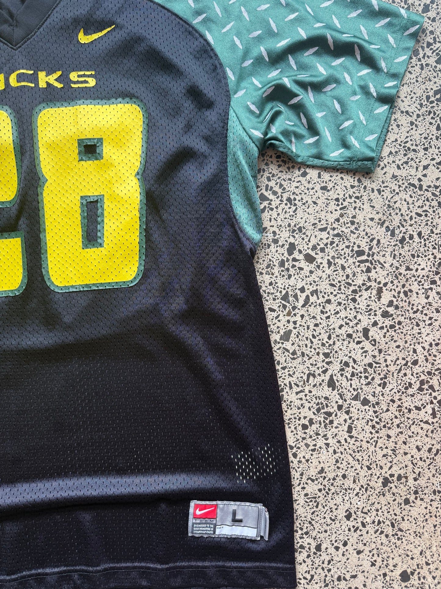 90s vintage Oregon Ducks jersey size L laid on polished concrete background — green with yellow detailing and Ducks logo.