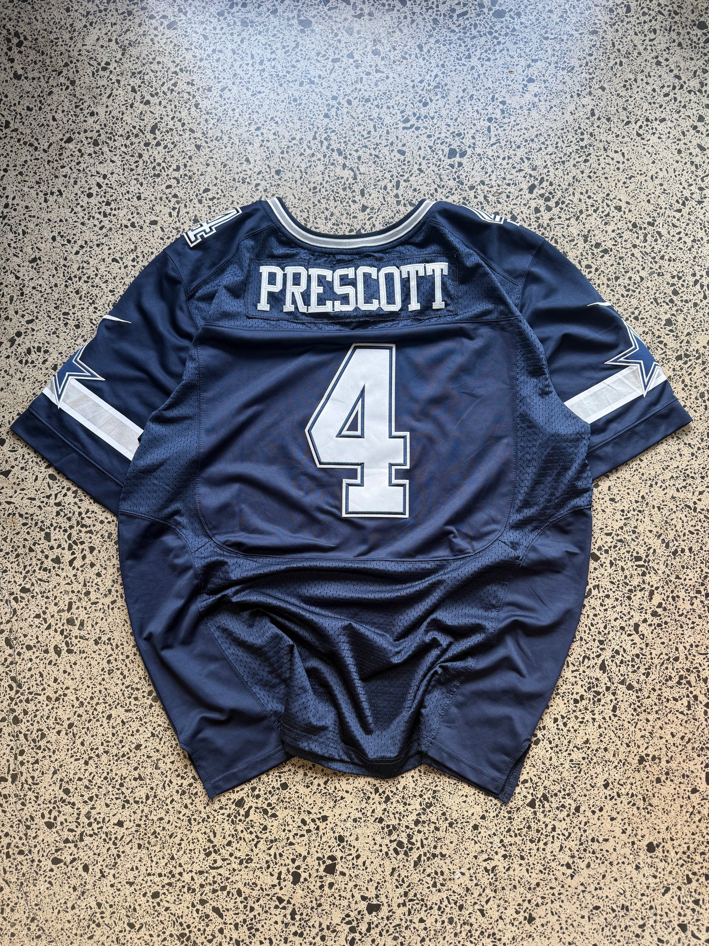 Dallas Cowboys Dak Prescott NFL jersey size 3XL laid on polished concrete background — navy with white detailing and star logo.