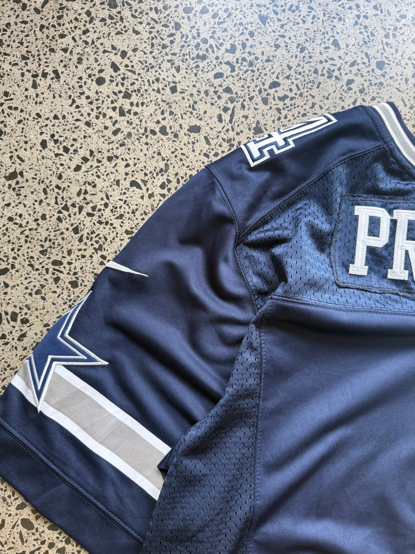 Dallas Cowboys Dak Prescott NFL jersey size 3XL laid on polished concrete background — navy with white detailing and star logo.