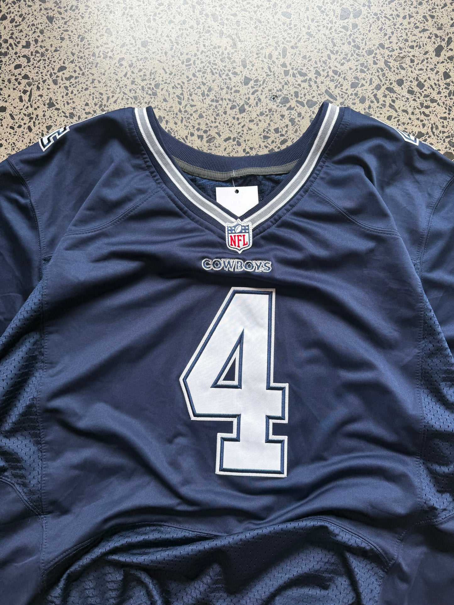 Dallas Cowboys Dak Prescott NFL jersey size 3XL laid on polished concrete background — navy with white detailing and star logo.