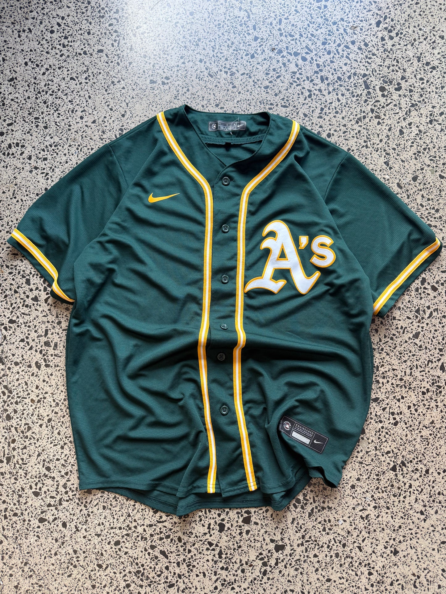 Nike Oakland Athletics MLB jersey size L laid on polished concrete background — green with yellow detailing and Nike logo.