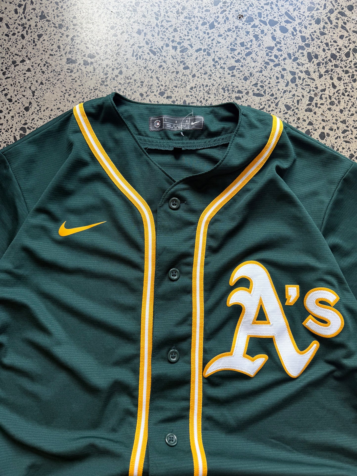 Nike Oakland Athletics MLB jersey size L laid on polished concrete background — green with yellow detailing and Nike logo.
