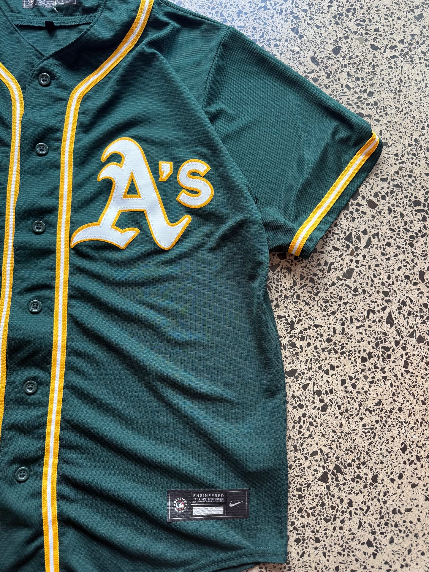 Nike Oakland Athletics MLB jersey size L laid on polished concrete background — green with yellow detailing and Nike logo.