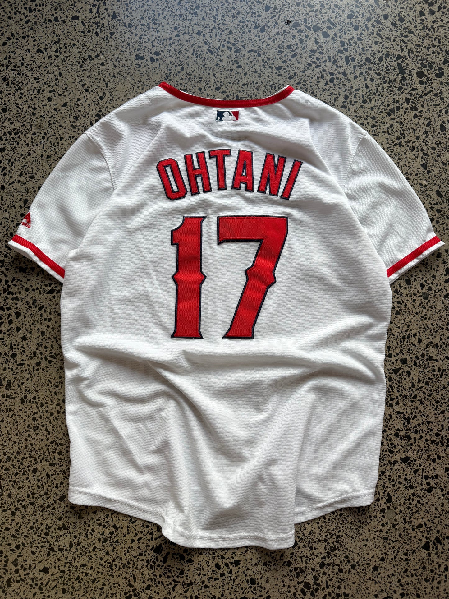 LA Angels Shohei Ohtani MLB baseball jersey size XL laid on polished concrete background — red with white detailing and Angels logo.