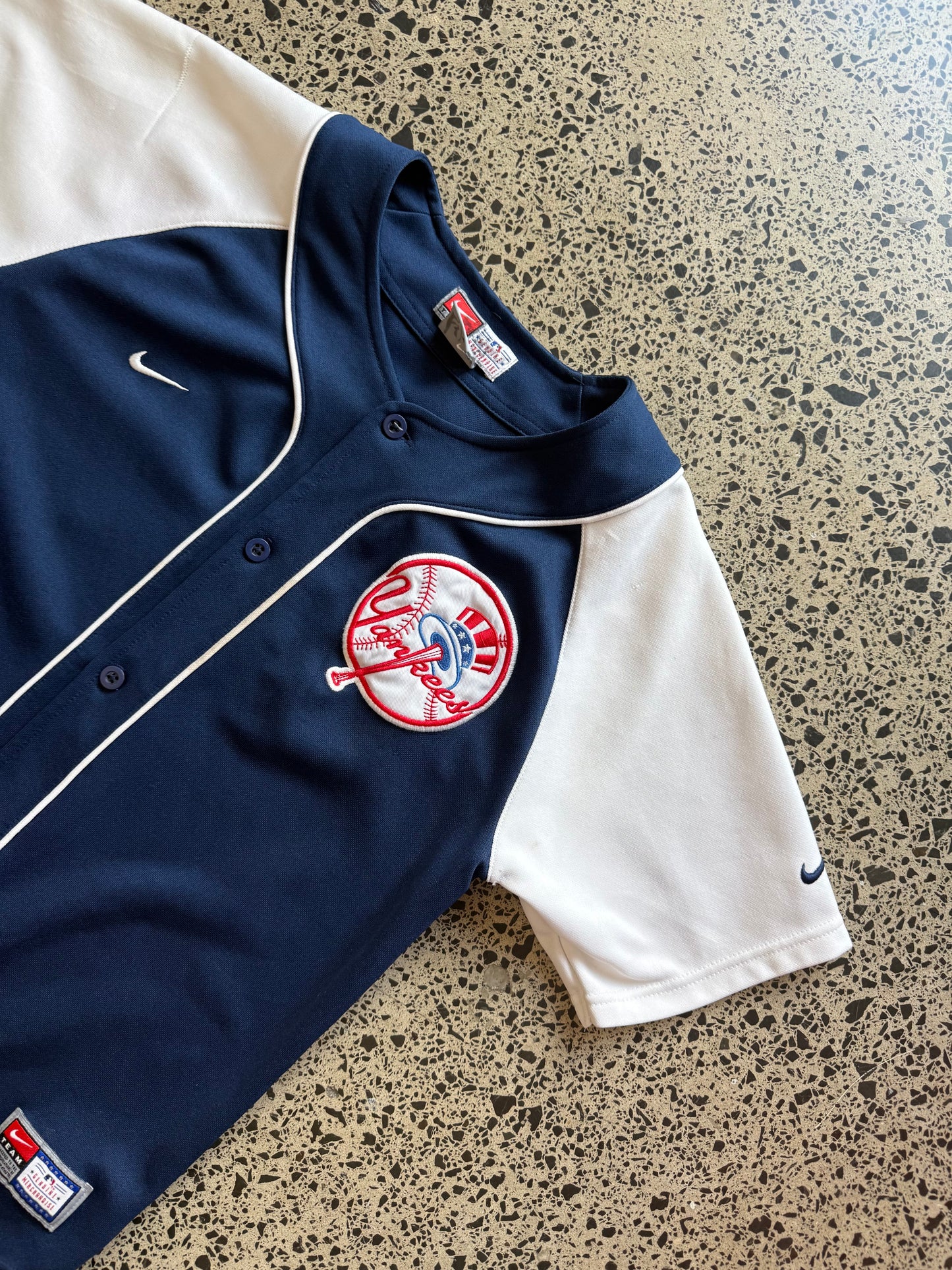New York Yankees MLB baseball jersey size M laid on polished concrete background — classic navy and white club colours with bold lettering.
