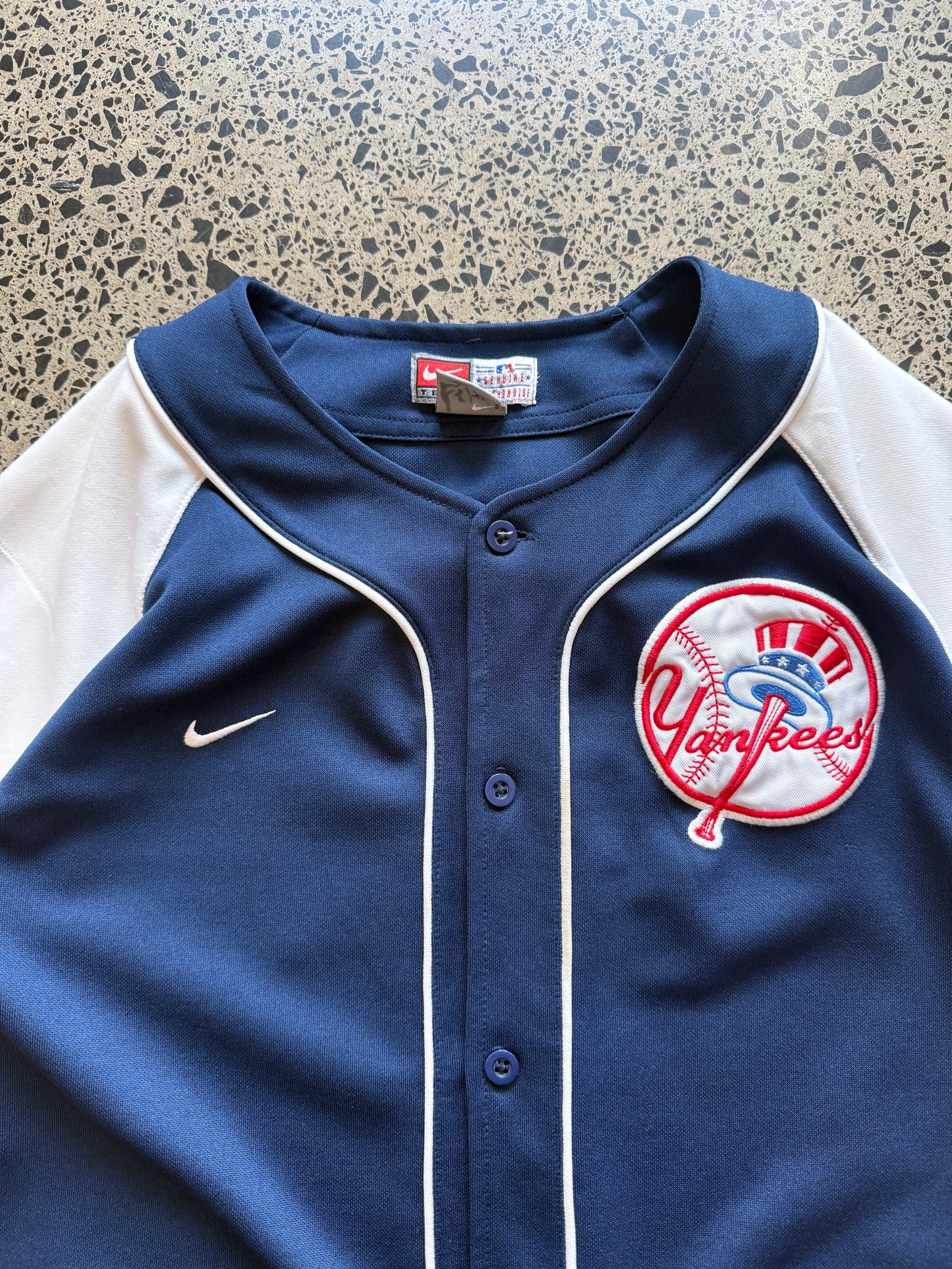 New York Yankees MLB baseball jersey size M laid on polished concrete background — classic navy and white club colours with bold lettering.