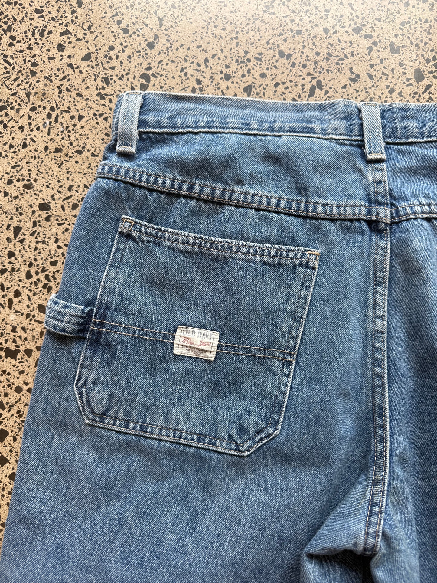 Old Navy dark blue wash denim jorts, size 34W, laid on polished concrete background. Knee cut with classic stitching and soft wash