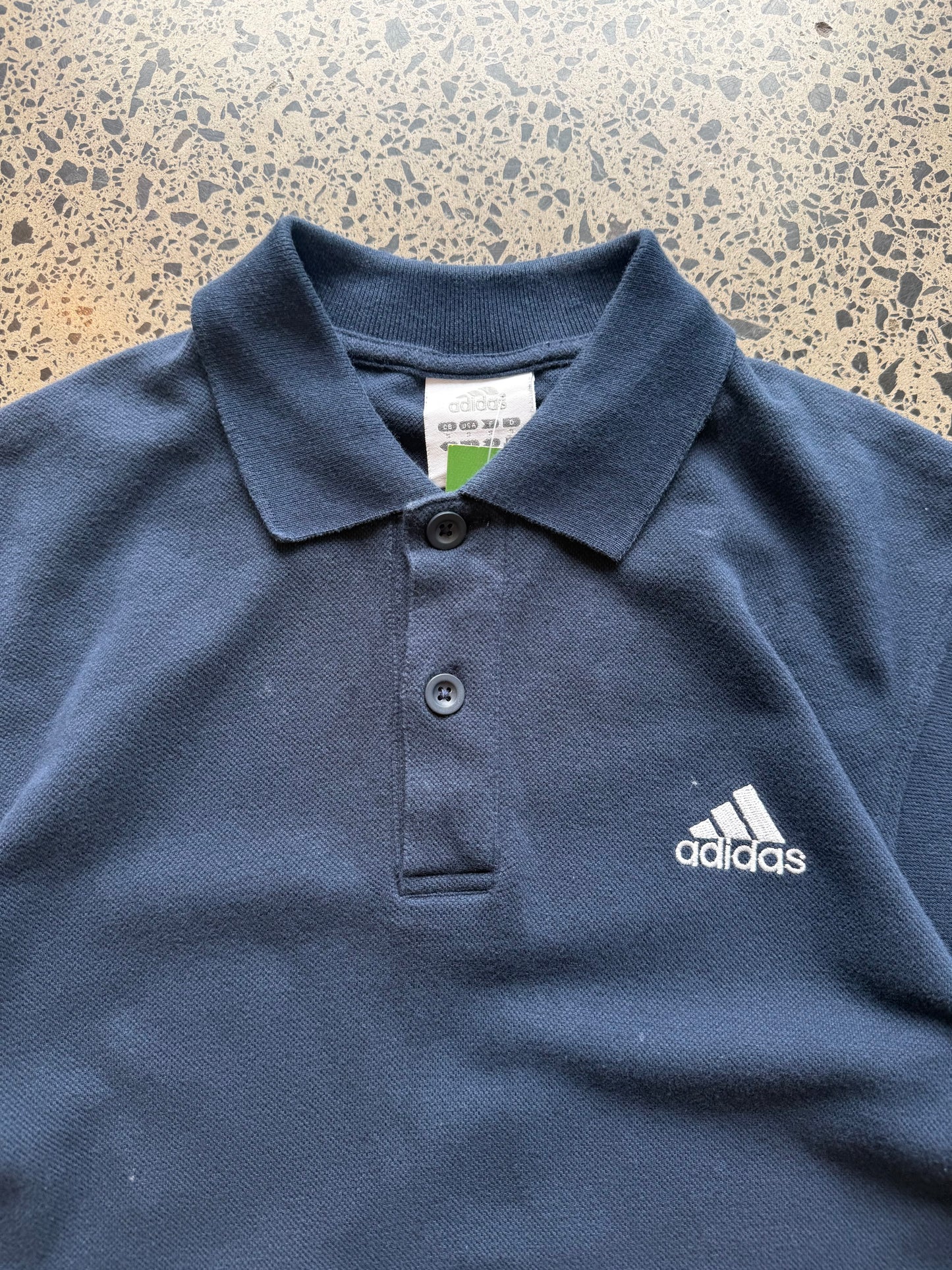 2000s Adidas polo shirt in size S laid flat on a polished concrete background featuring classic Adidas branding and a collared design.