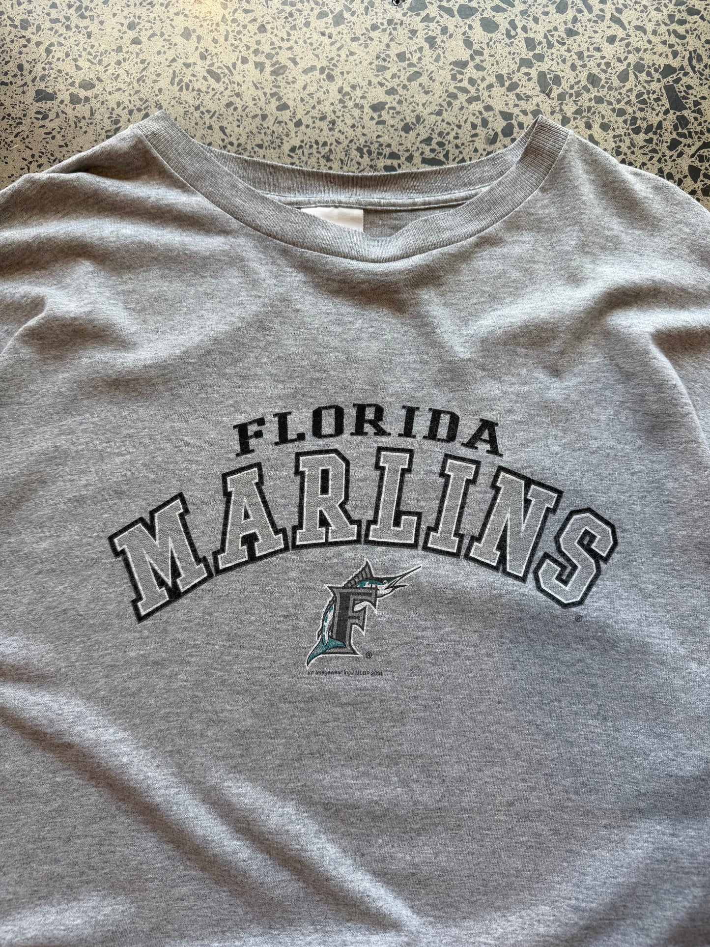 2004 Florida Marlins baseball T-shirt, size 2XL, laid on polished concrete background with early-2000s MLB graphic.