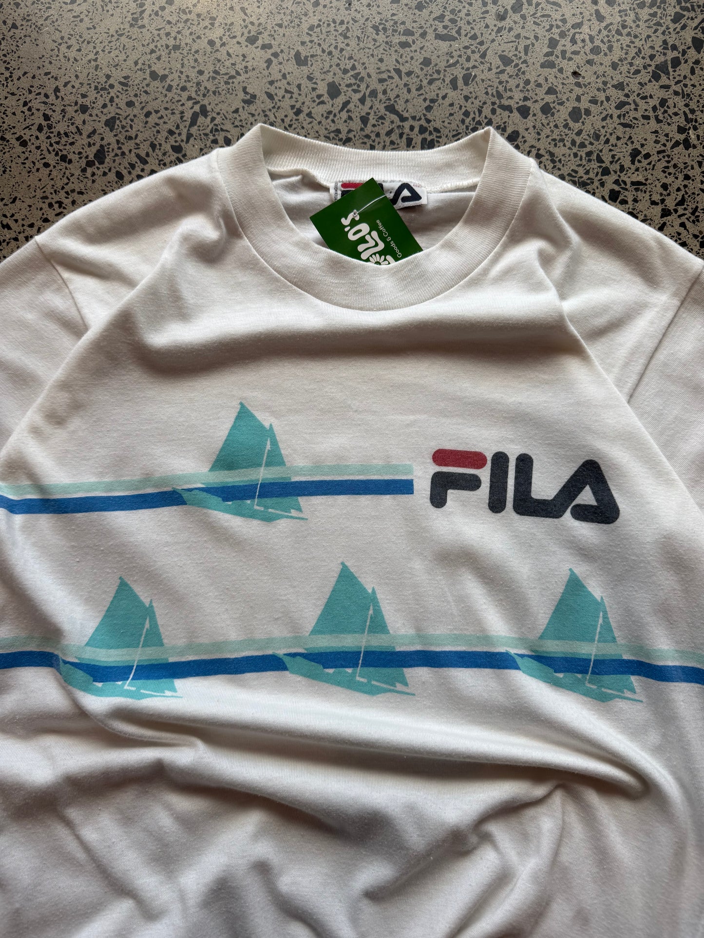 90s Fila graphic T-shirt, size L, laid on polished concrete background — vintage cotton tee with bold Fila logo print.