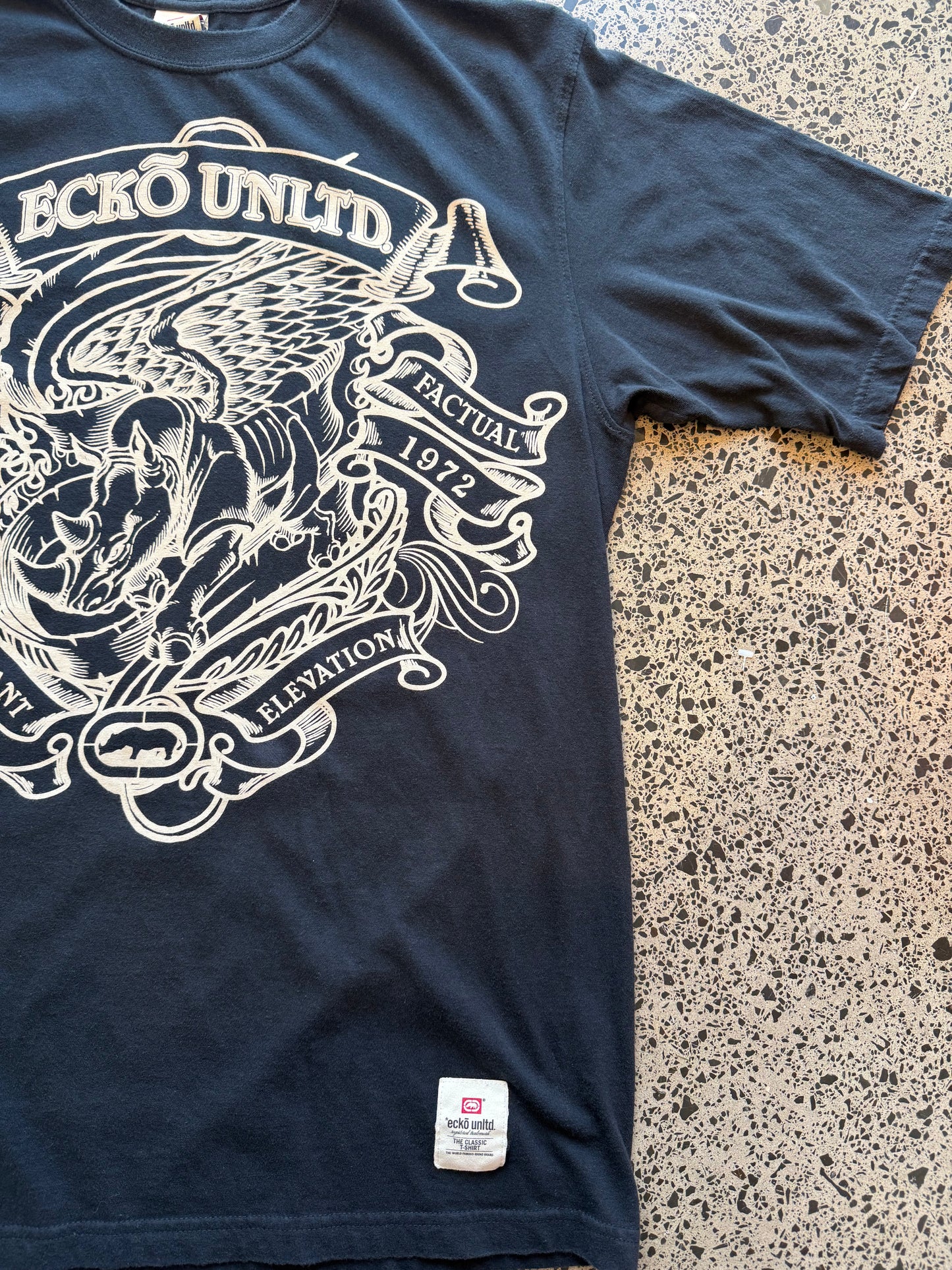 Ecko Unltd black graphic T-shirt size XL laid on polished concrete background — bold Y2K-style print on soft black cotton.