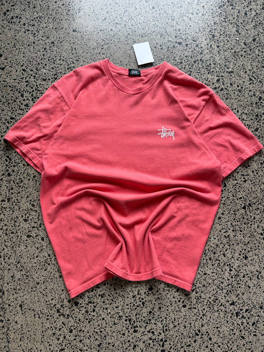 Stussy salmon graphic T-shirt, size L, laid on polished concrete background — bold front logo on soft salmon cotton.