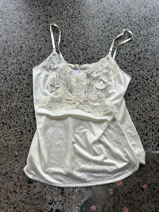 White satin camisole with lace detailing on a textured surface
