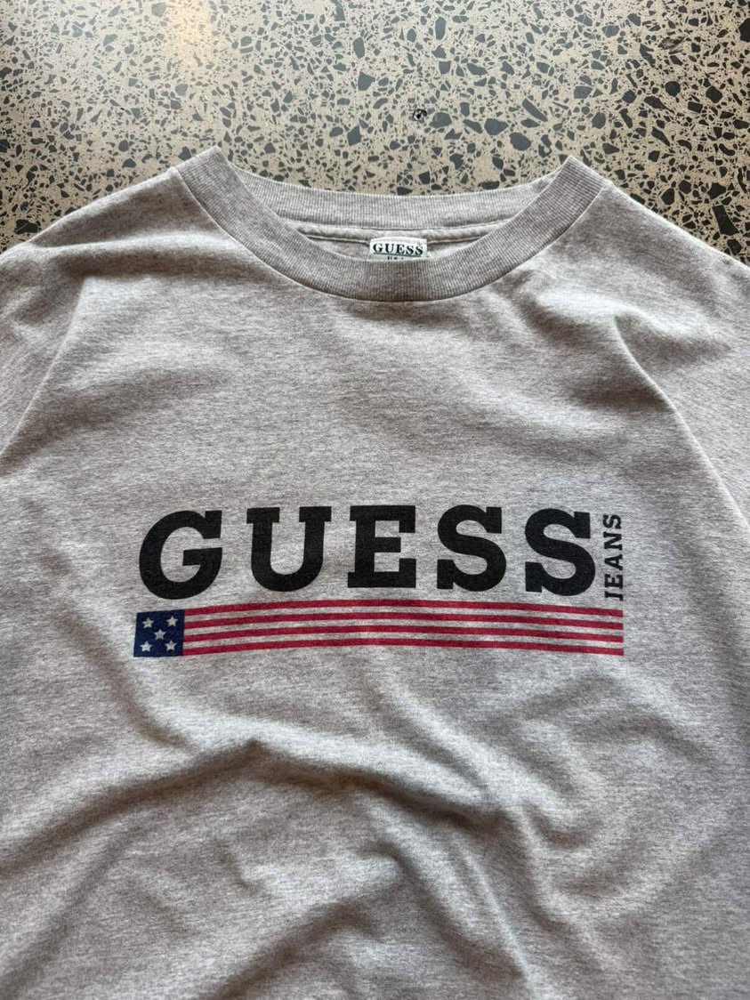 90s Guess Jeans graphic T-shirt in size XL laid flat on a polished concrete background featuring classic logo branding.
