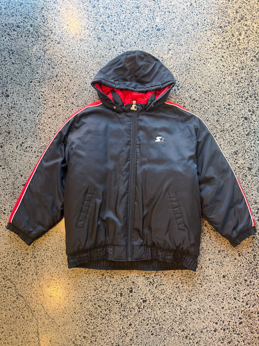 90s black and red Starter jacket size M laid flat on polished concrete background, vintage jacket with bold colour blocking and classic Starter fit.