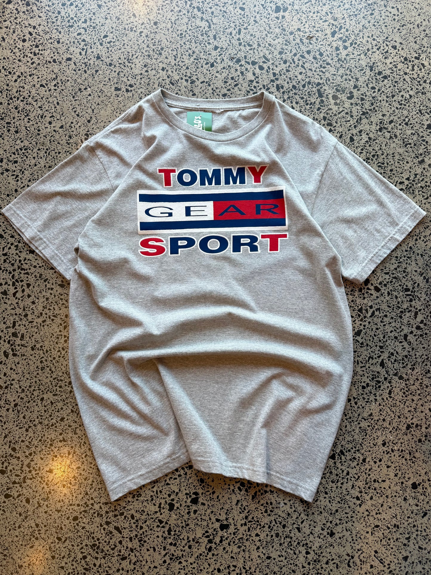 2000s Tommy Hilfiger T-shirt in size L laid on a polished concrete background with small front logo.